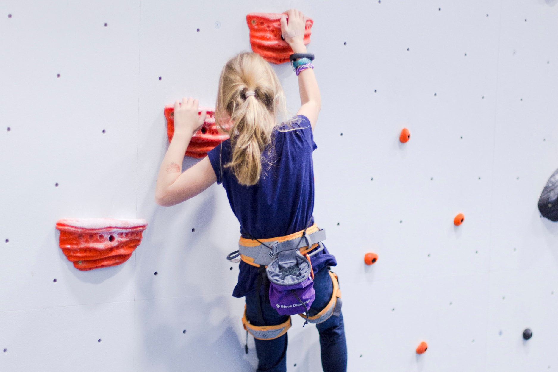 A young girl boulders on jugs.