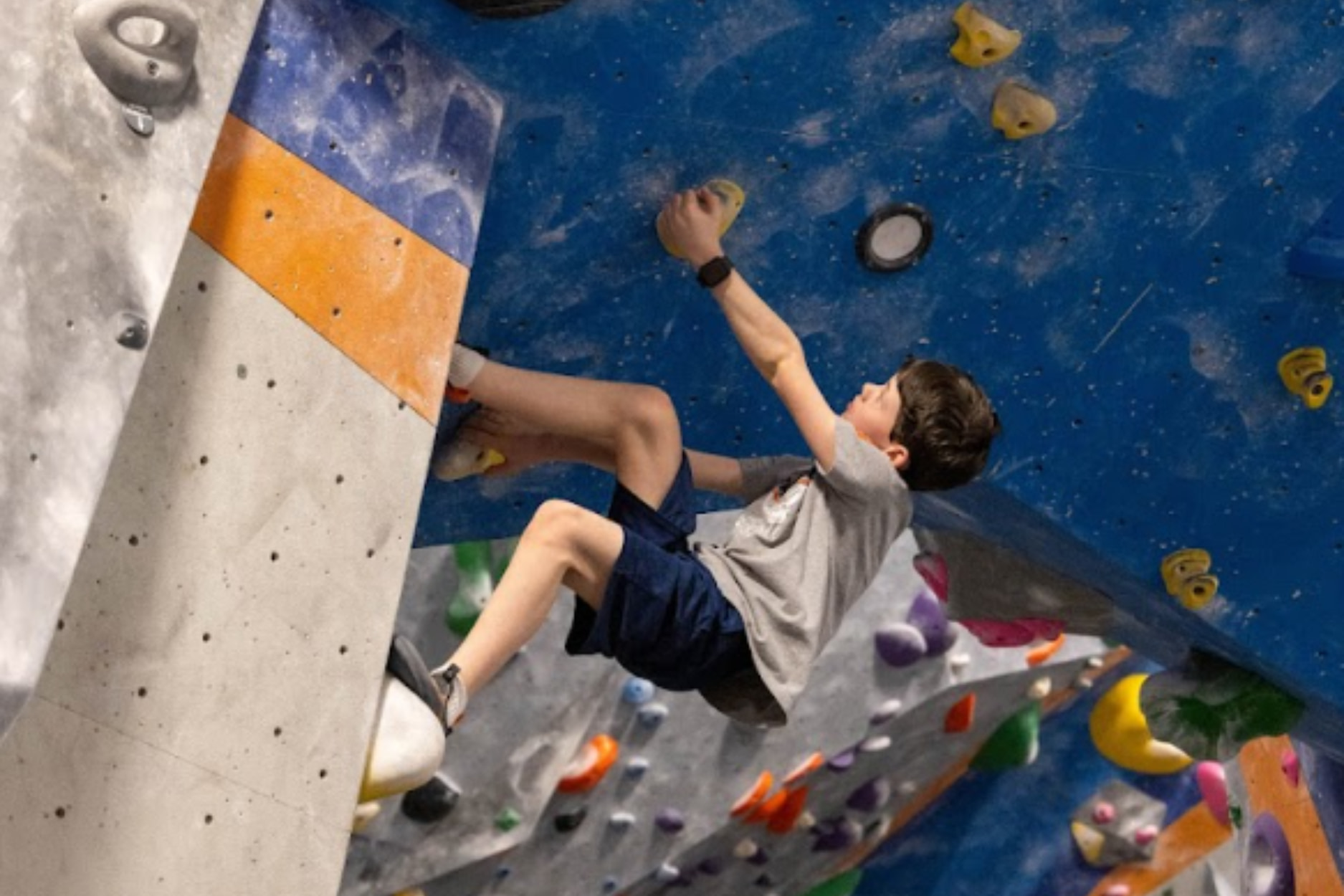 A young boy is bouldering on a steep wall.