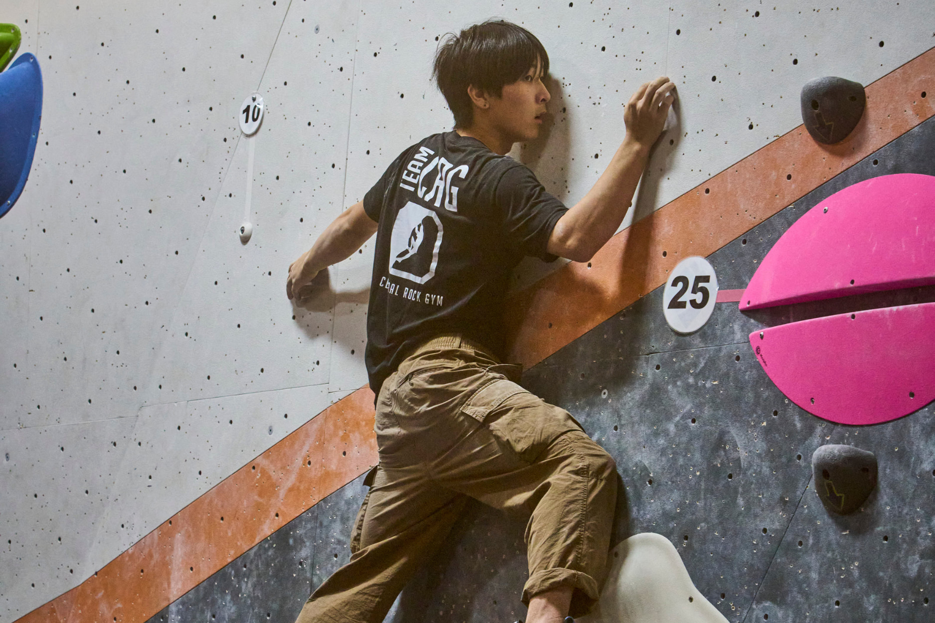 An older boy wearing a team CRG shirt is balancing on a slab boulder at a climbing competition