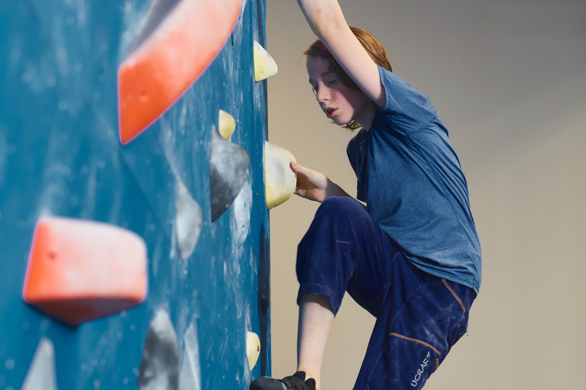 A teen boy climbs a boulder.