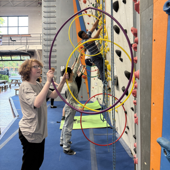 Kids climbing and kids holding hula hoops up against the climbing wall for a climbing challenge!