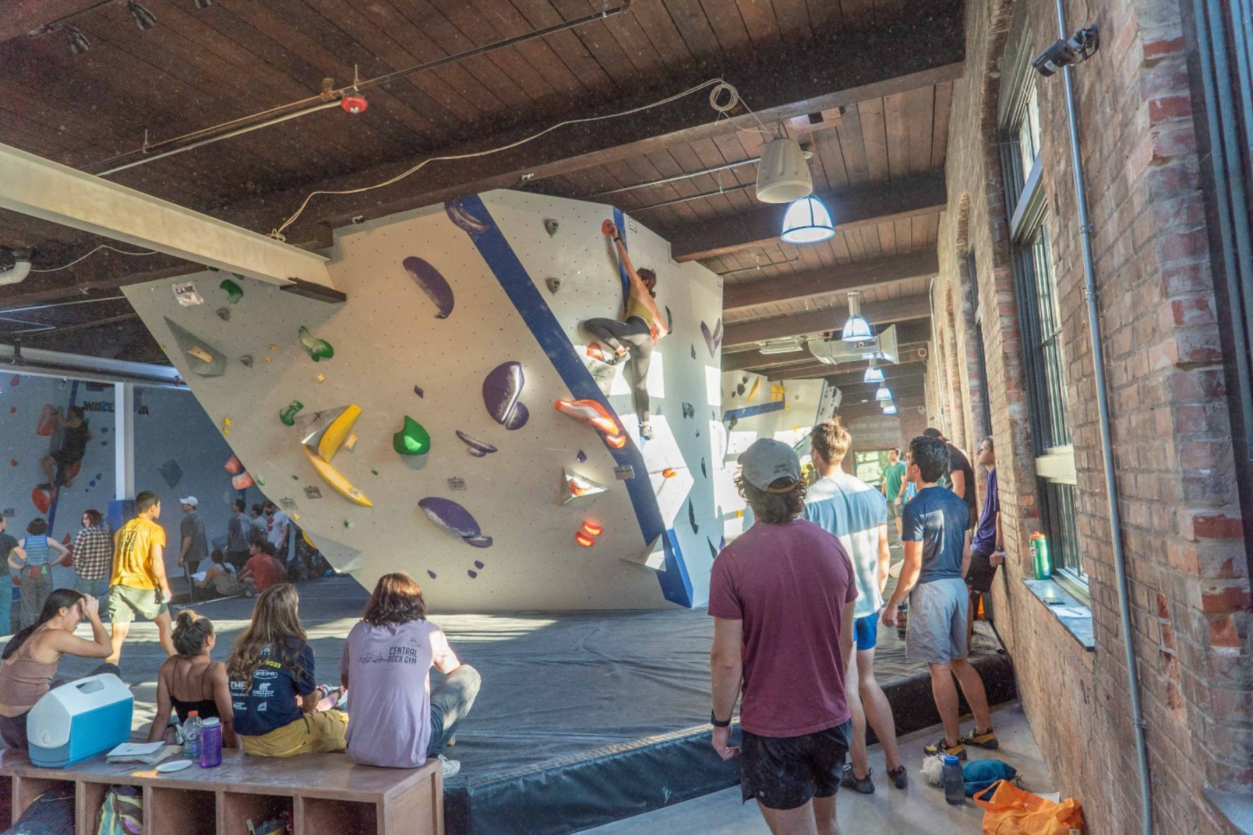 Climbers and spectators watch a competitor attempt a boulder problem during Boulders & Brews at Central Rock Gym Syracuse.