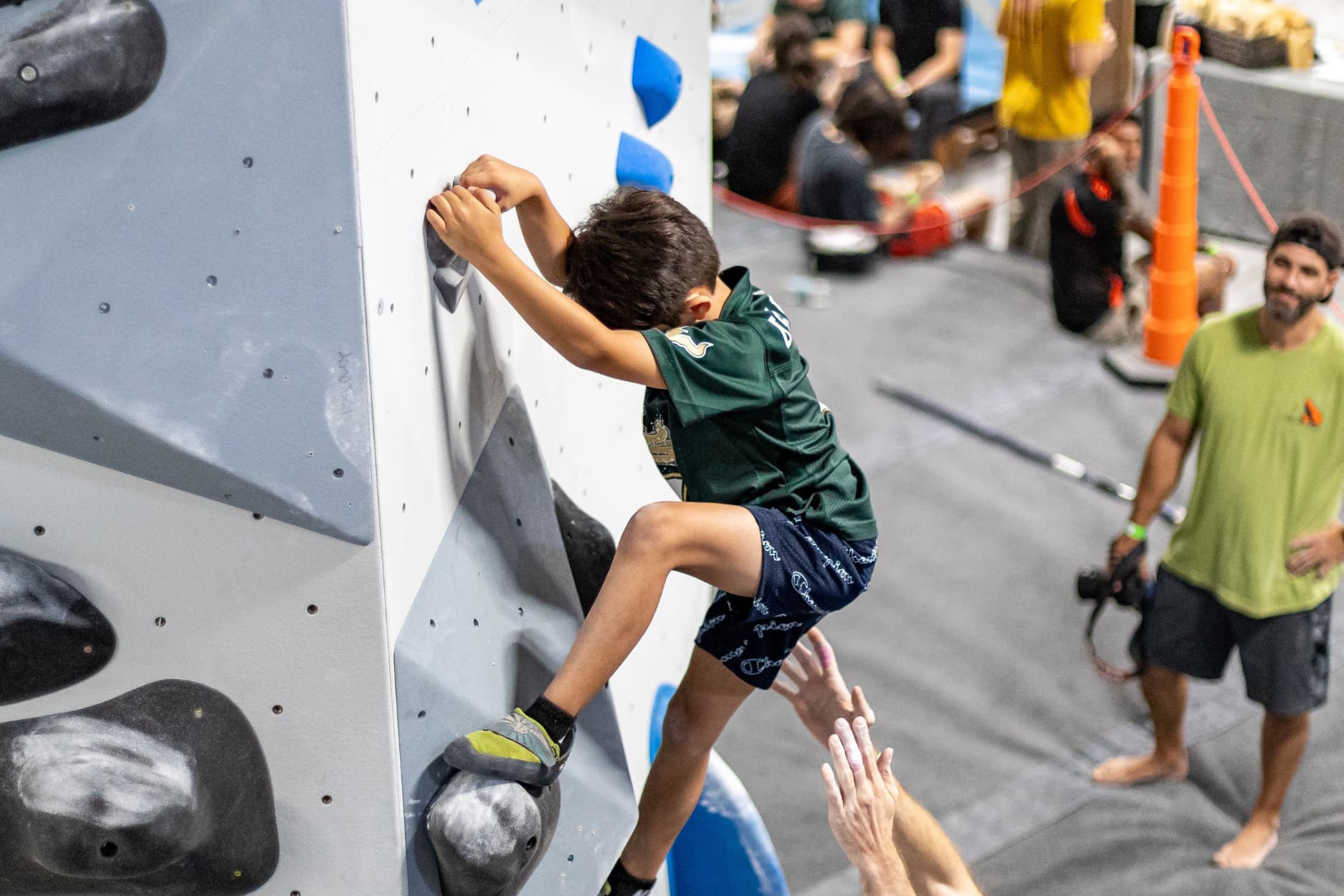 A young boy holds onto a down climb jug after completing a climb and looks down at his feet as he decends.