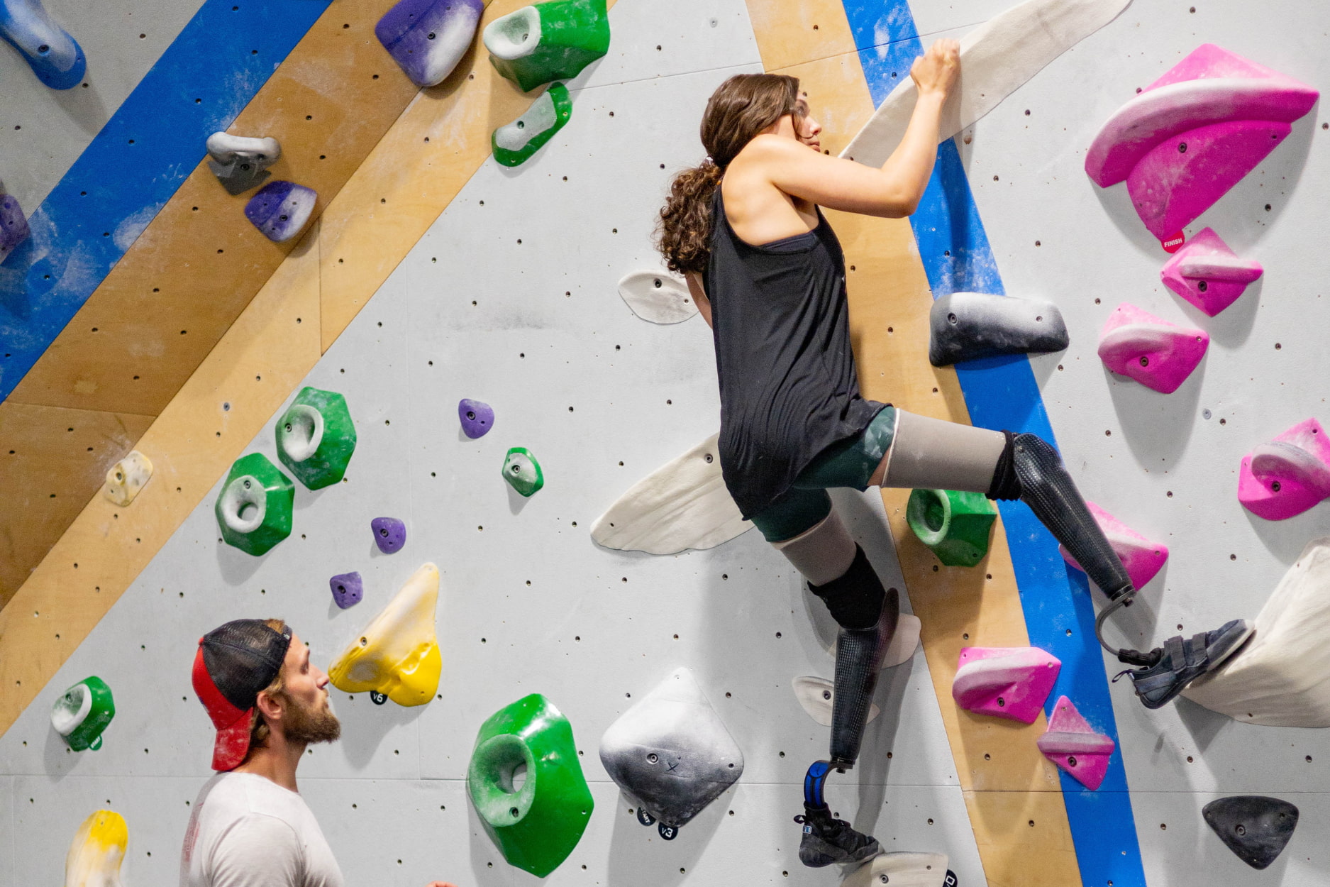 An adaptive climber boulders. She has an amputation above the knee for both legs and climbs with two prosthetic legs.