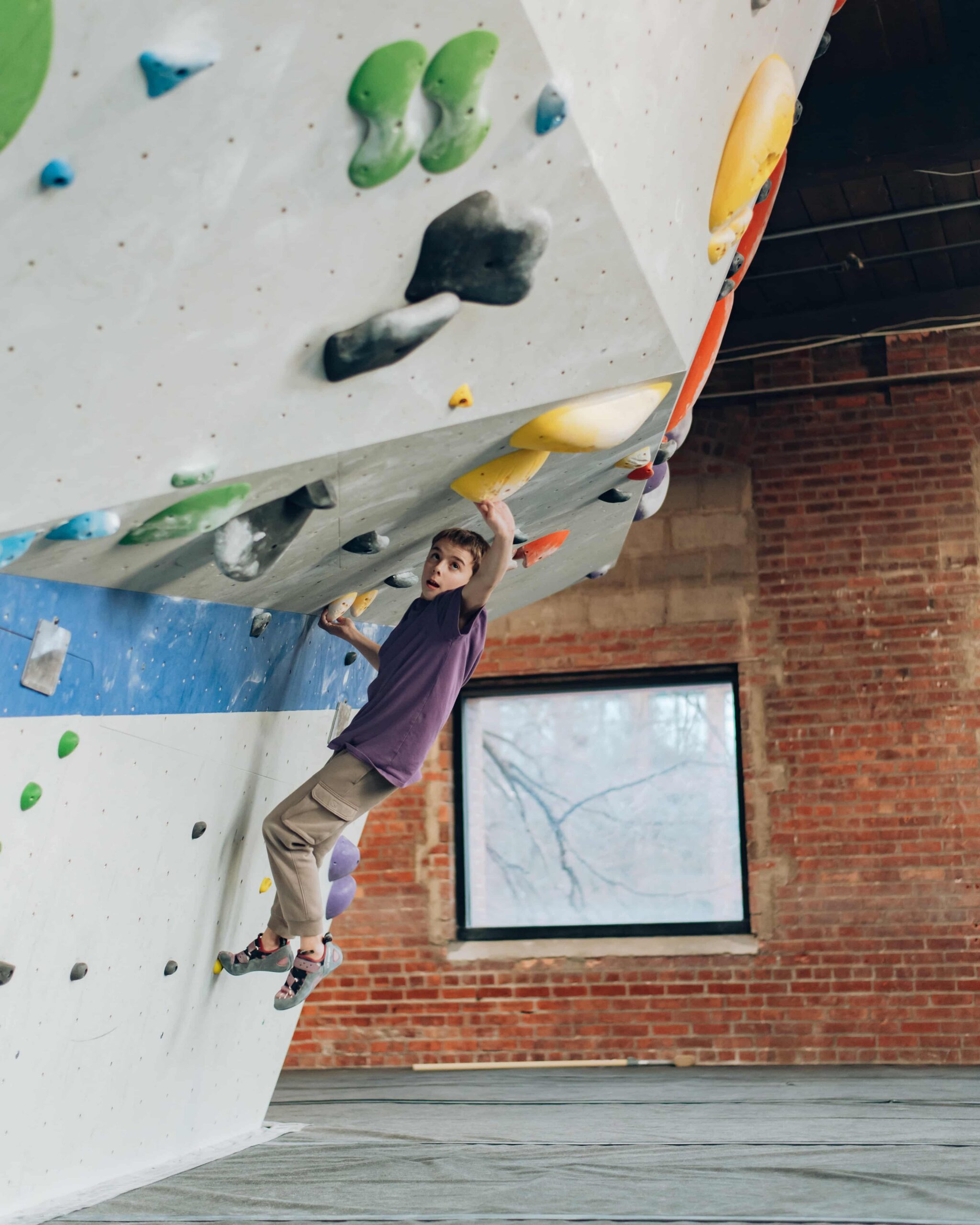 A young boy boulders on an overhang.