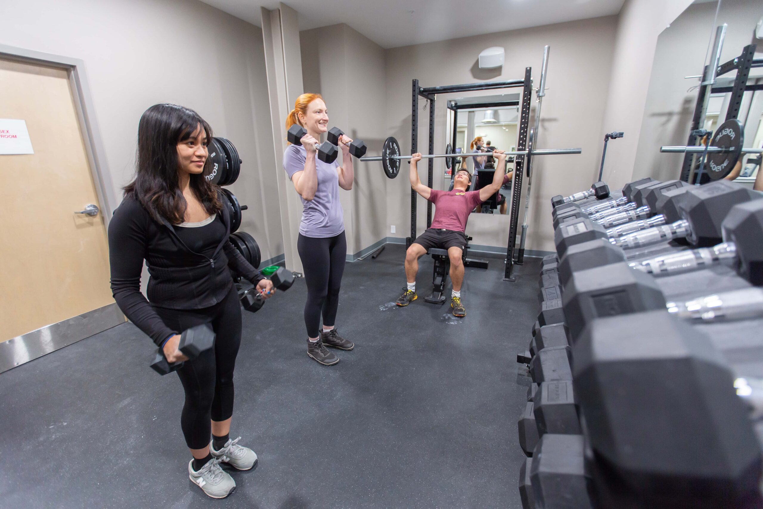 Two women and a man lift weights in the gym.