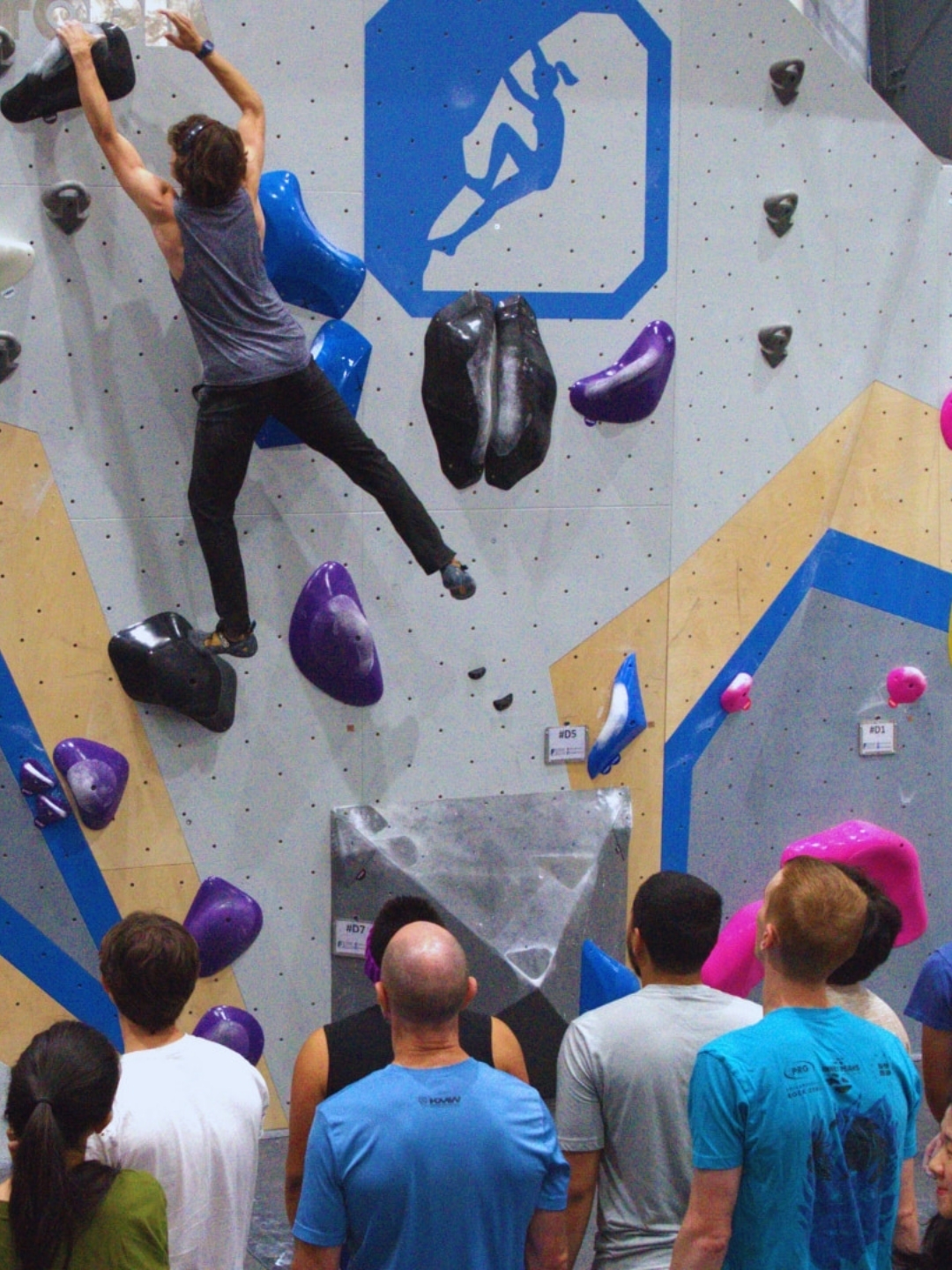 A crowd watches eagerly as a climber dynos to the finish.