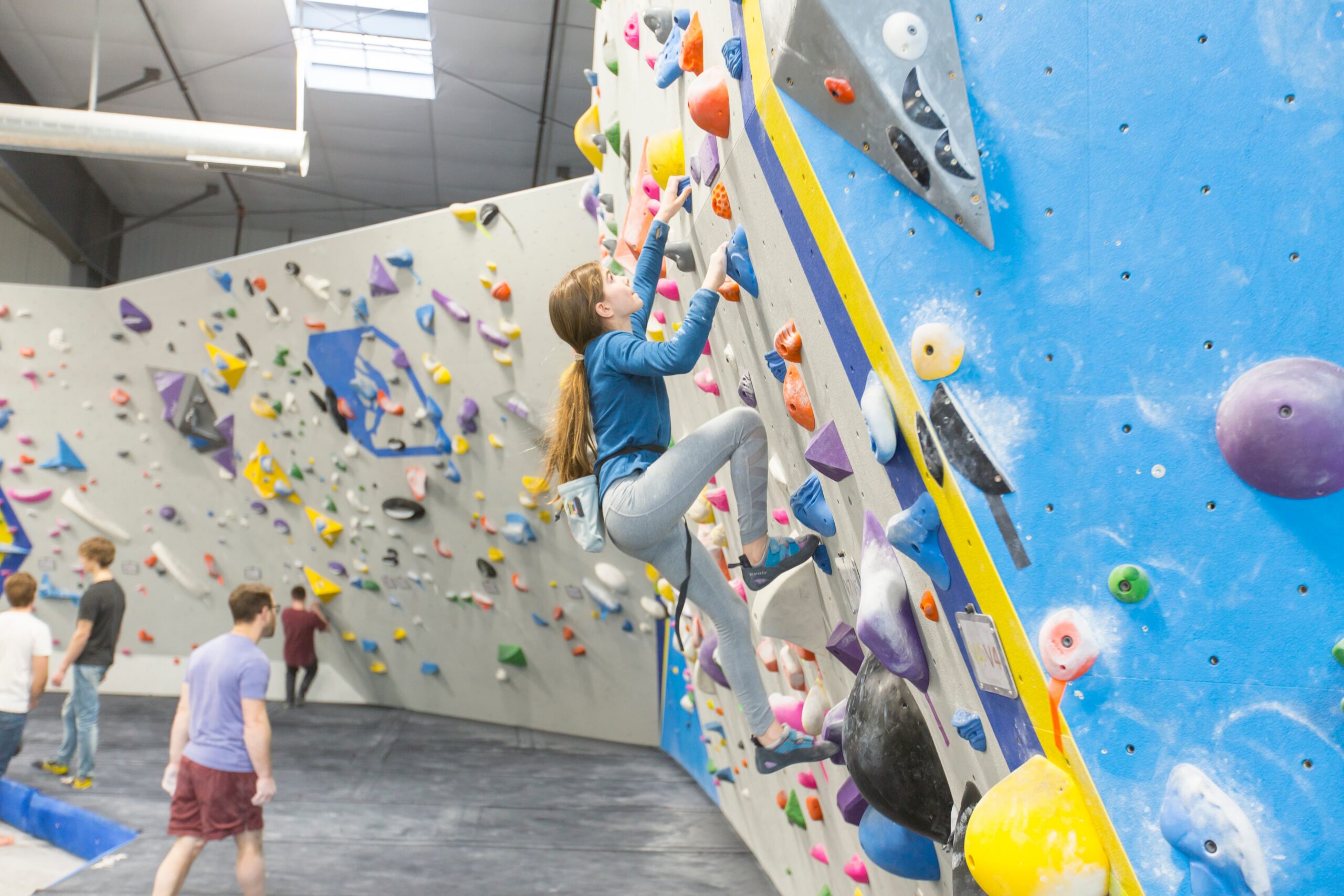 A young teenage girl is bouldering. She is focused on making a big move.