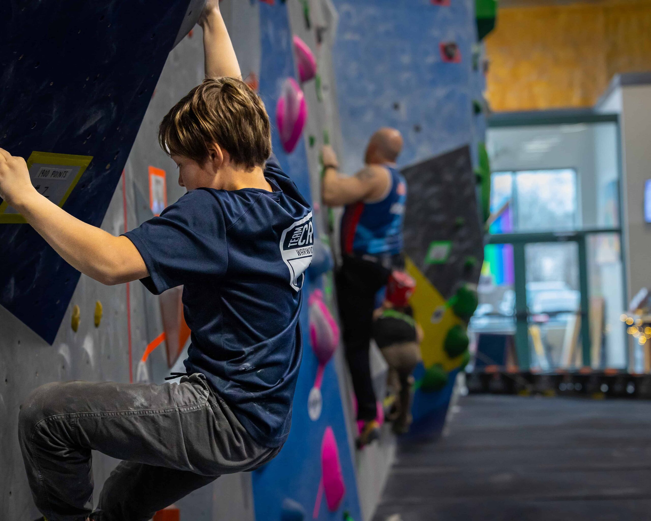 A teen boy wearing a team CRG t-shirt is bouldering.