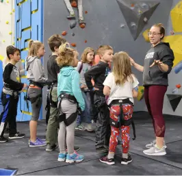 A group of young children huddle together near the bouldering wall with an instructor in black during a kids' group event at Central Rock Gym Watertown.