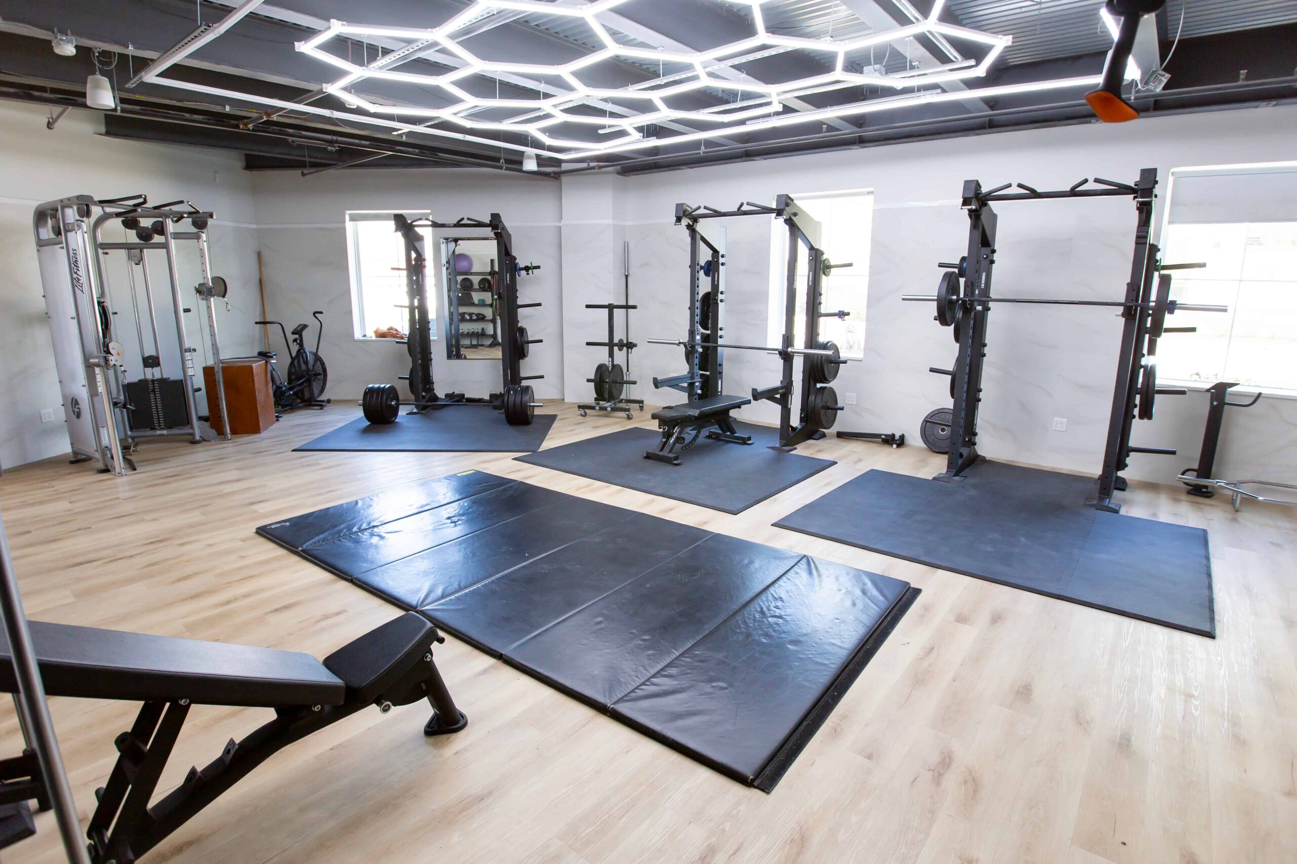 A brightly lit fitness area with a cable machine and multiple squat racks.
