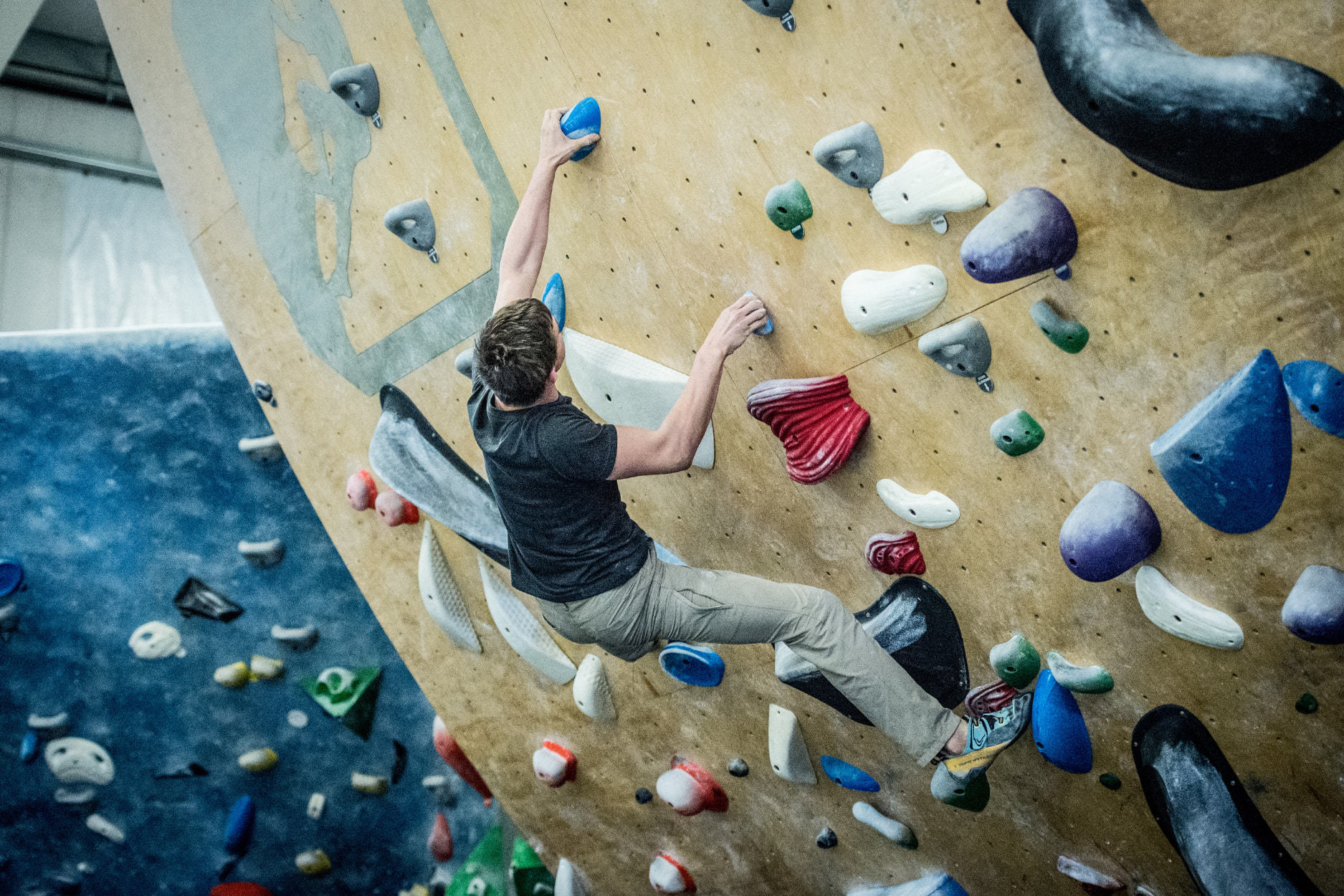 An older teen boy boulders and grabs hold of a pinch on an overhanging wall.
