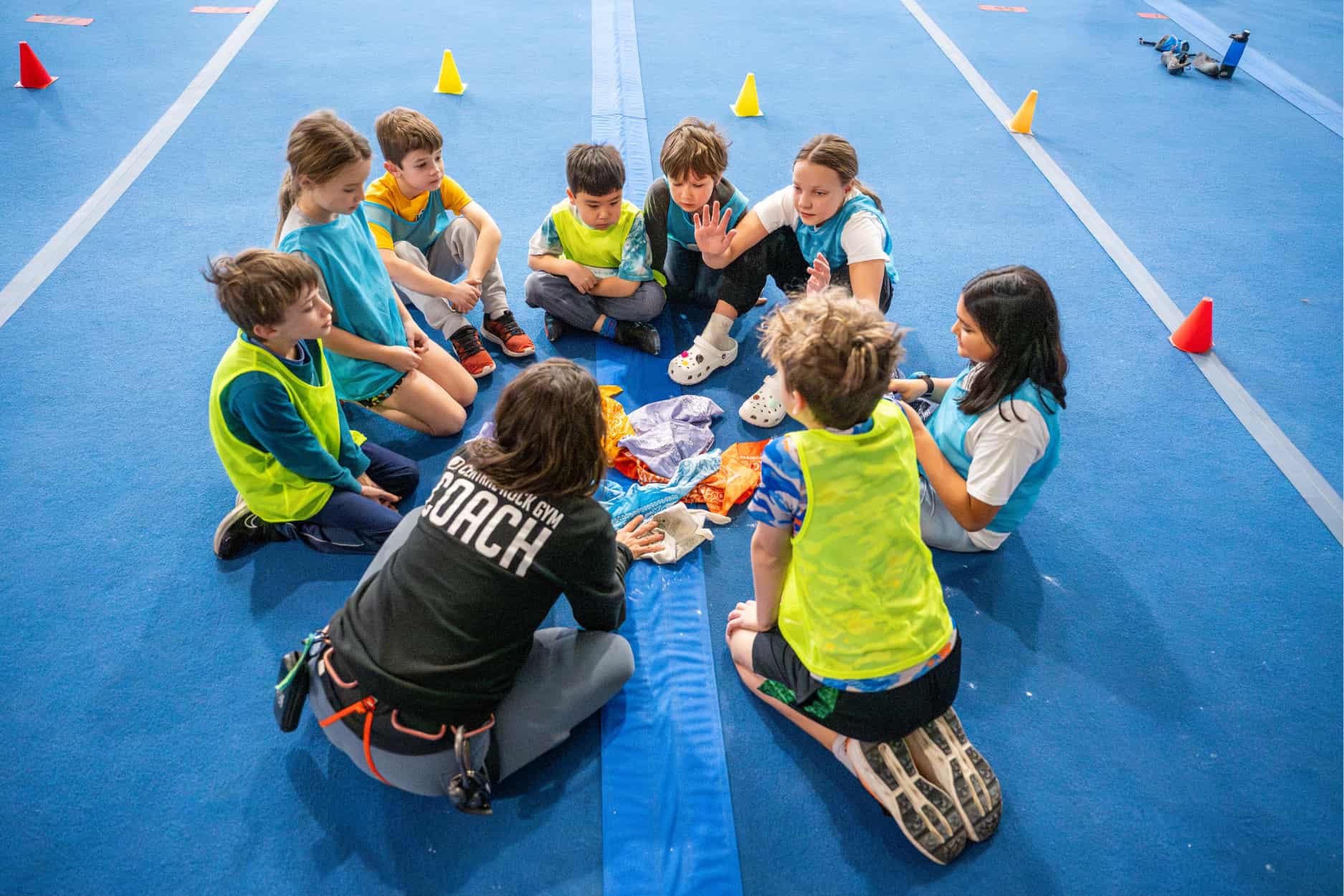 A group of campers sit with a Central Rock Gym climbing coach in a circle during a vacation program.