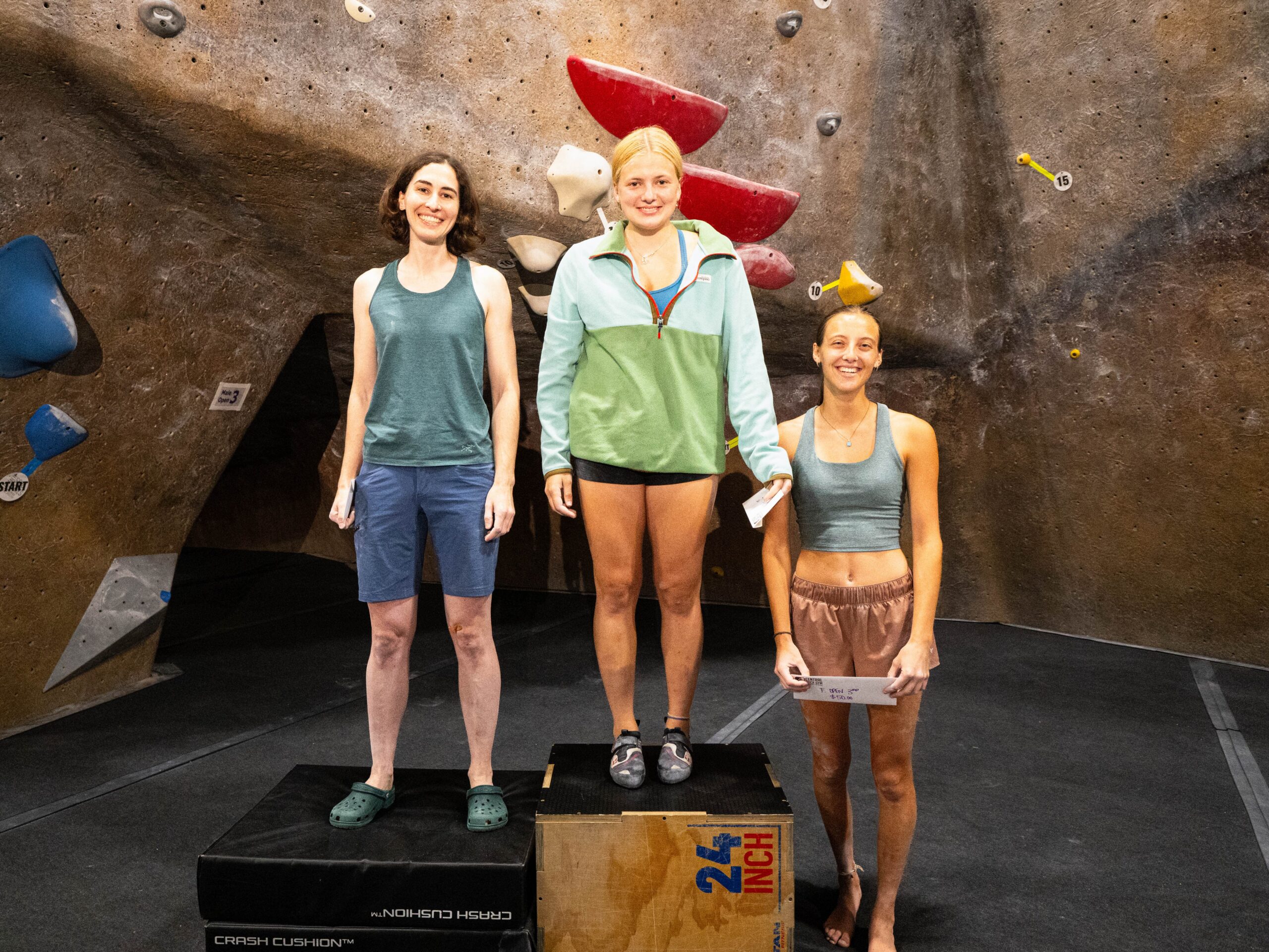 Three women stand on a winners podium at the Summer Send Series Finals at Central Rock Gym Hadley.
