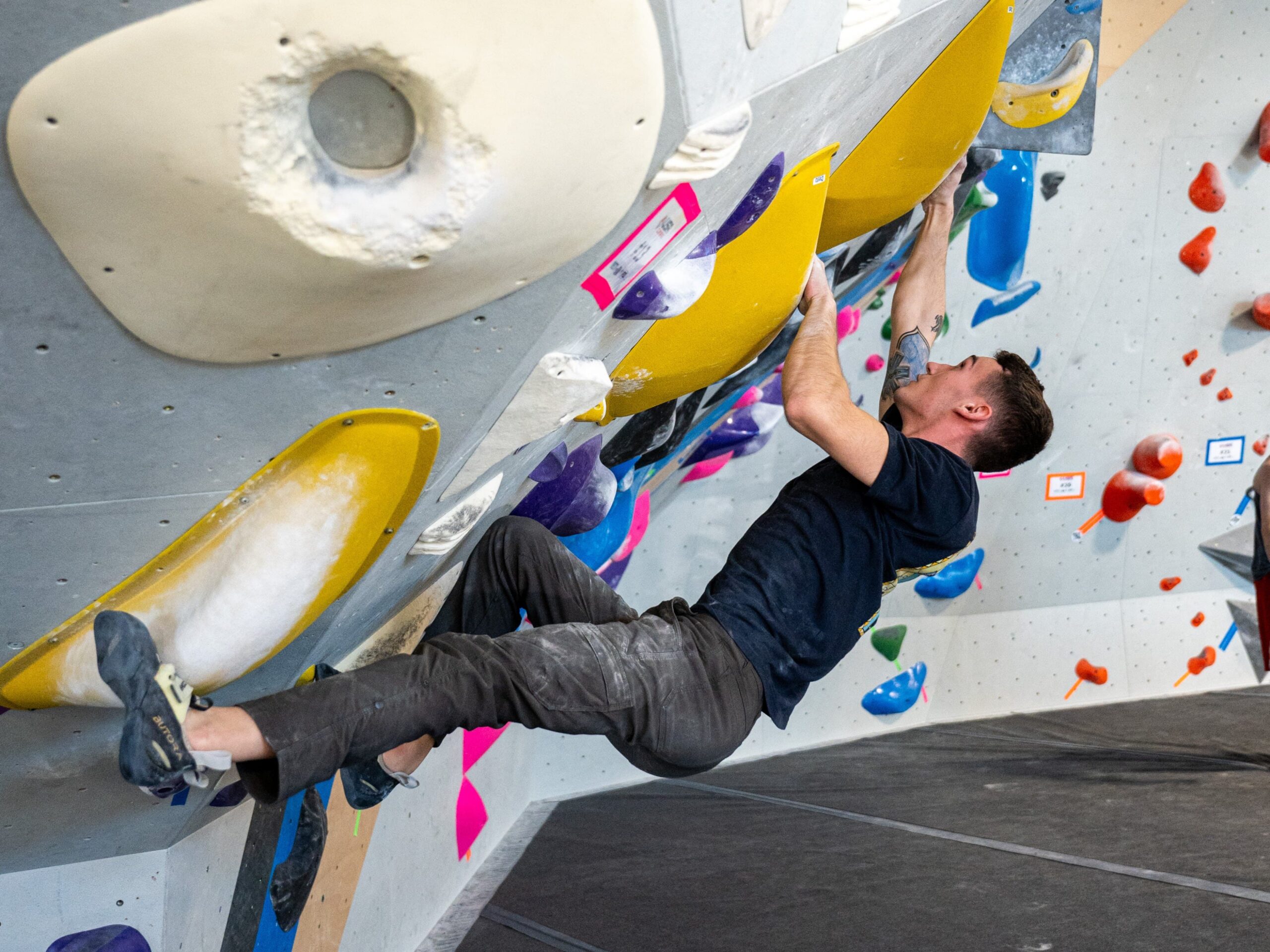 A man bouldering on an indoor climbing wall. The climbing holds are yellow and he is doing a toe hook.