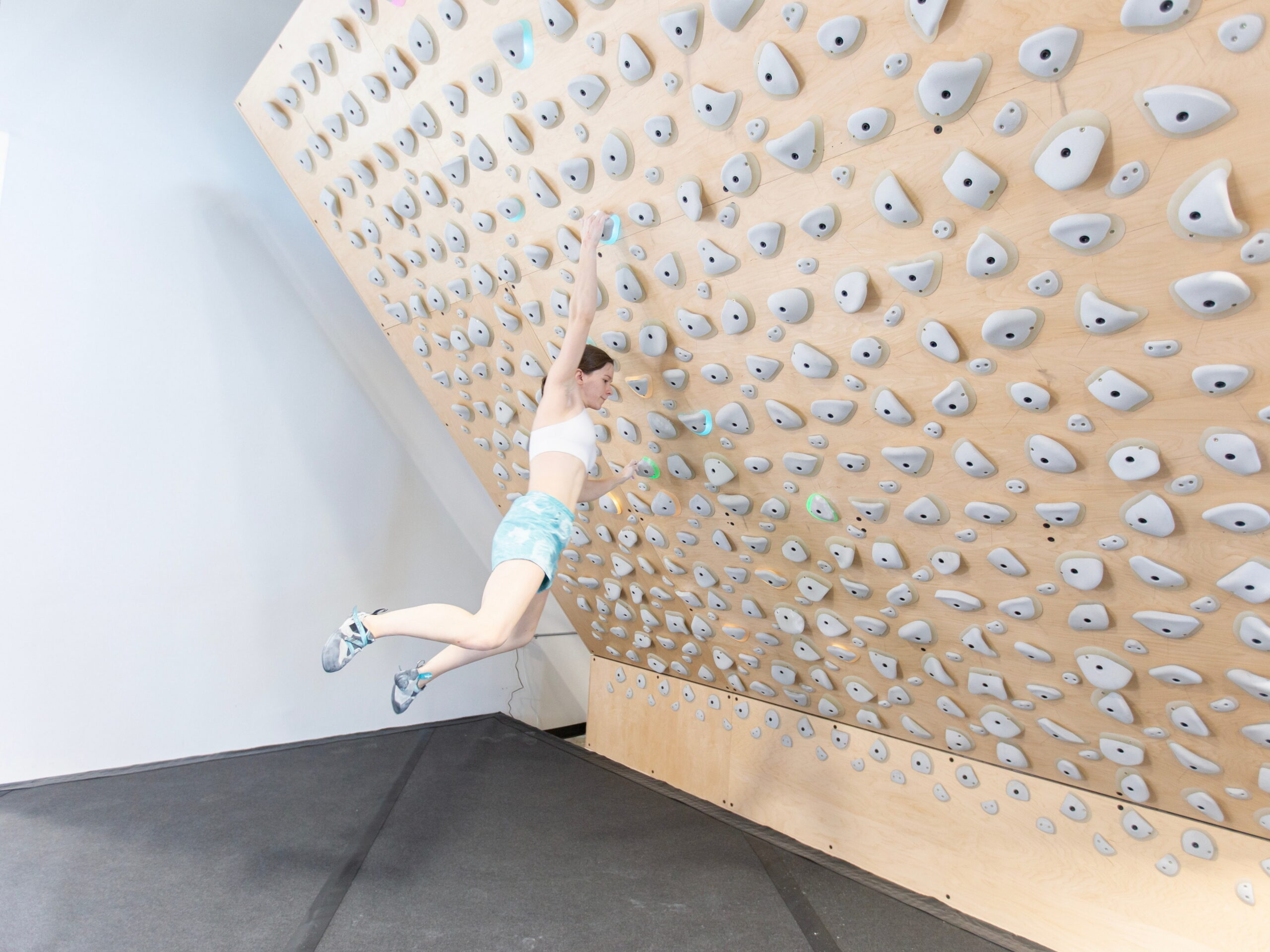 A woman climbing on a Kilter Board hanging onto climbing holds with just her arms.