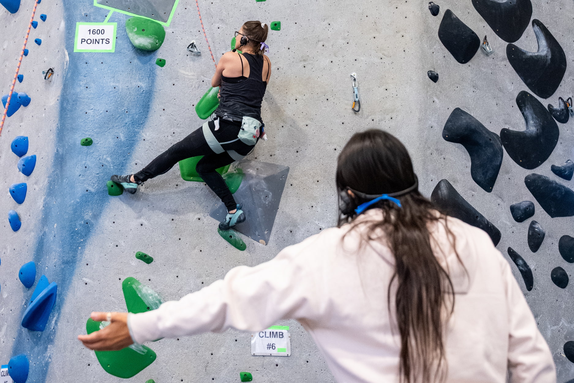 A blind climber is top rope climbing as their guide give directions for the next hold on the wall.
