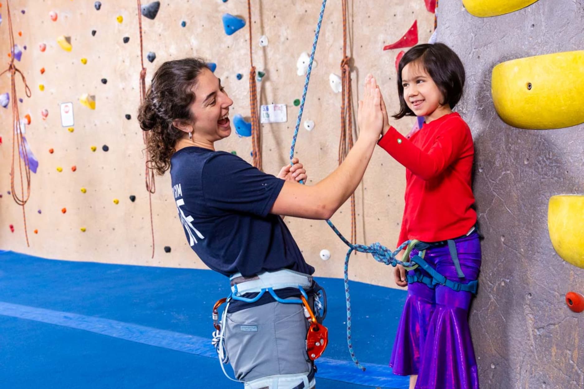 a girl is learning to climb and a instructor is giving her a high five her at central rock gym