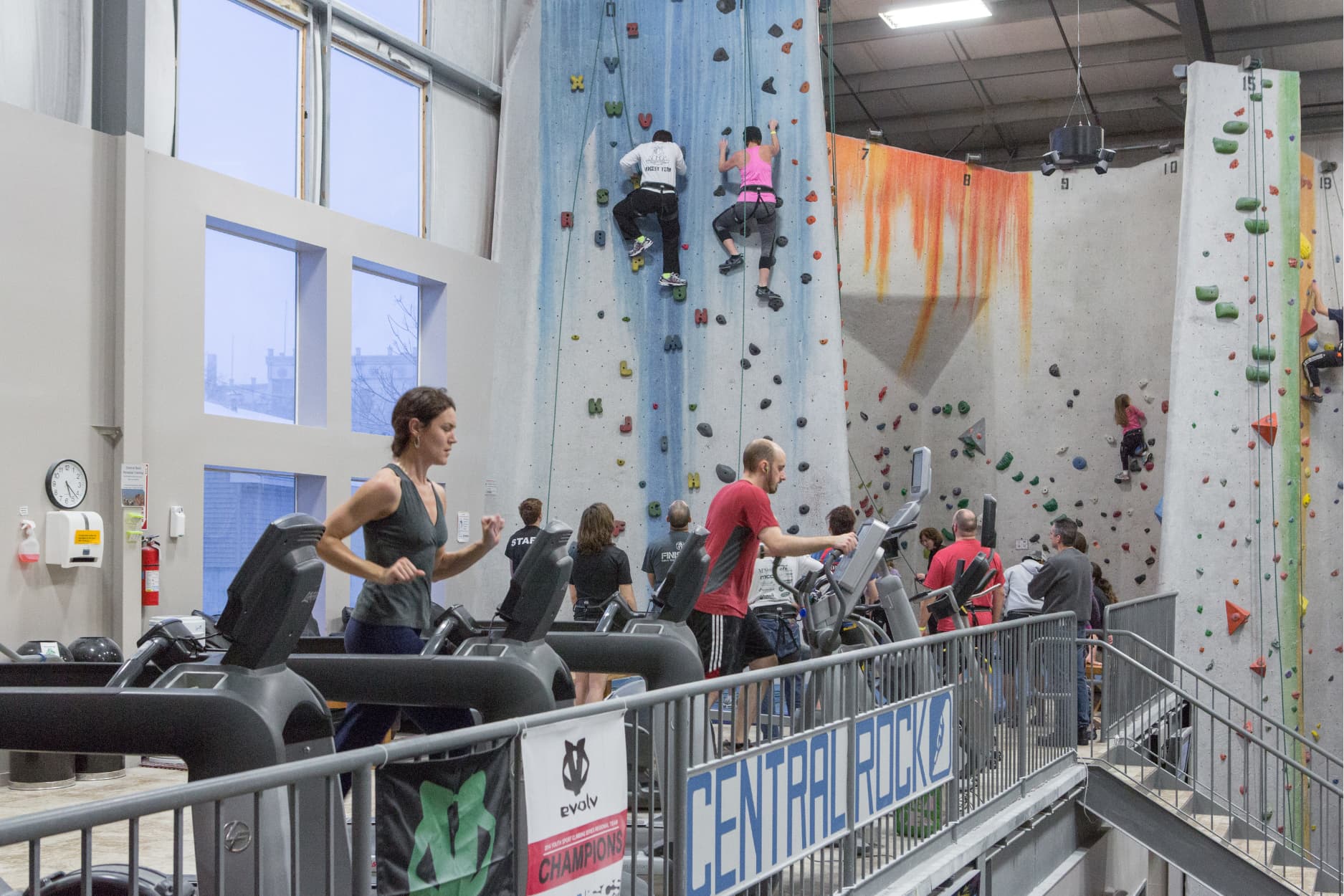 people doing cardio with people top rope climbing in the back at central rock gym