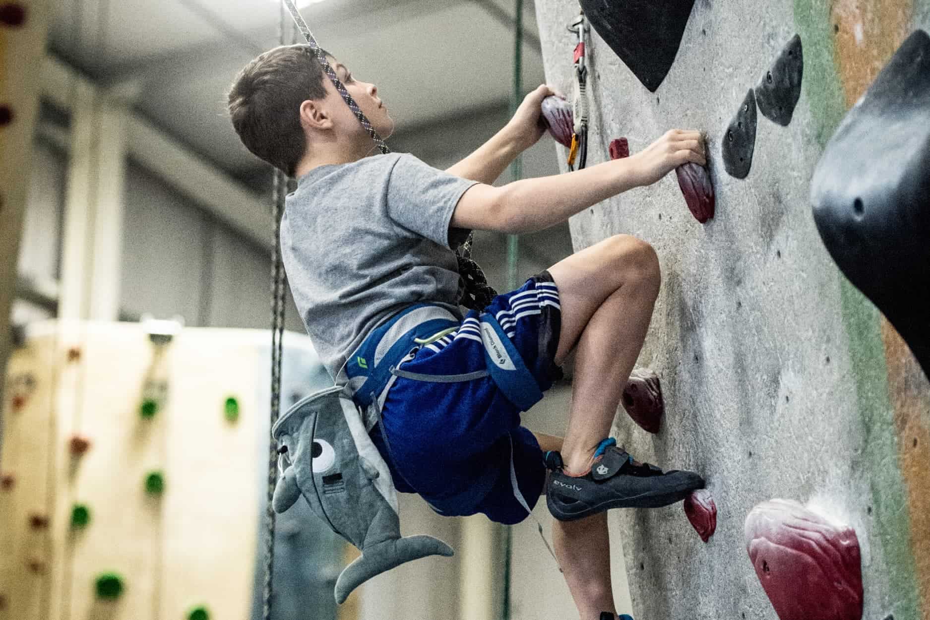 a young boy is top rope climbing at central rock gym