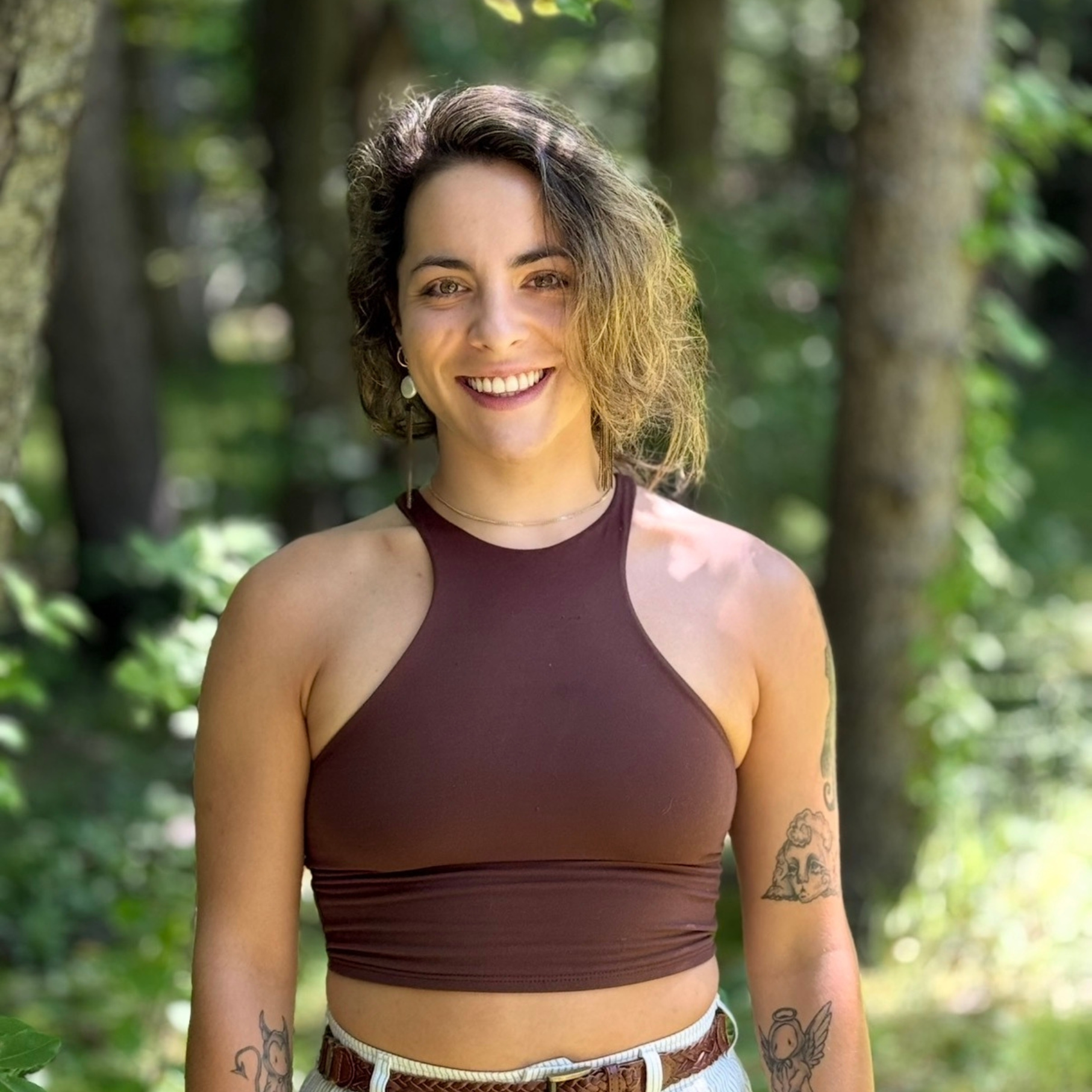 A woman stands and poses for a photo in the woods.