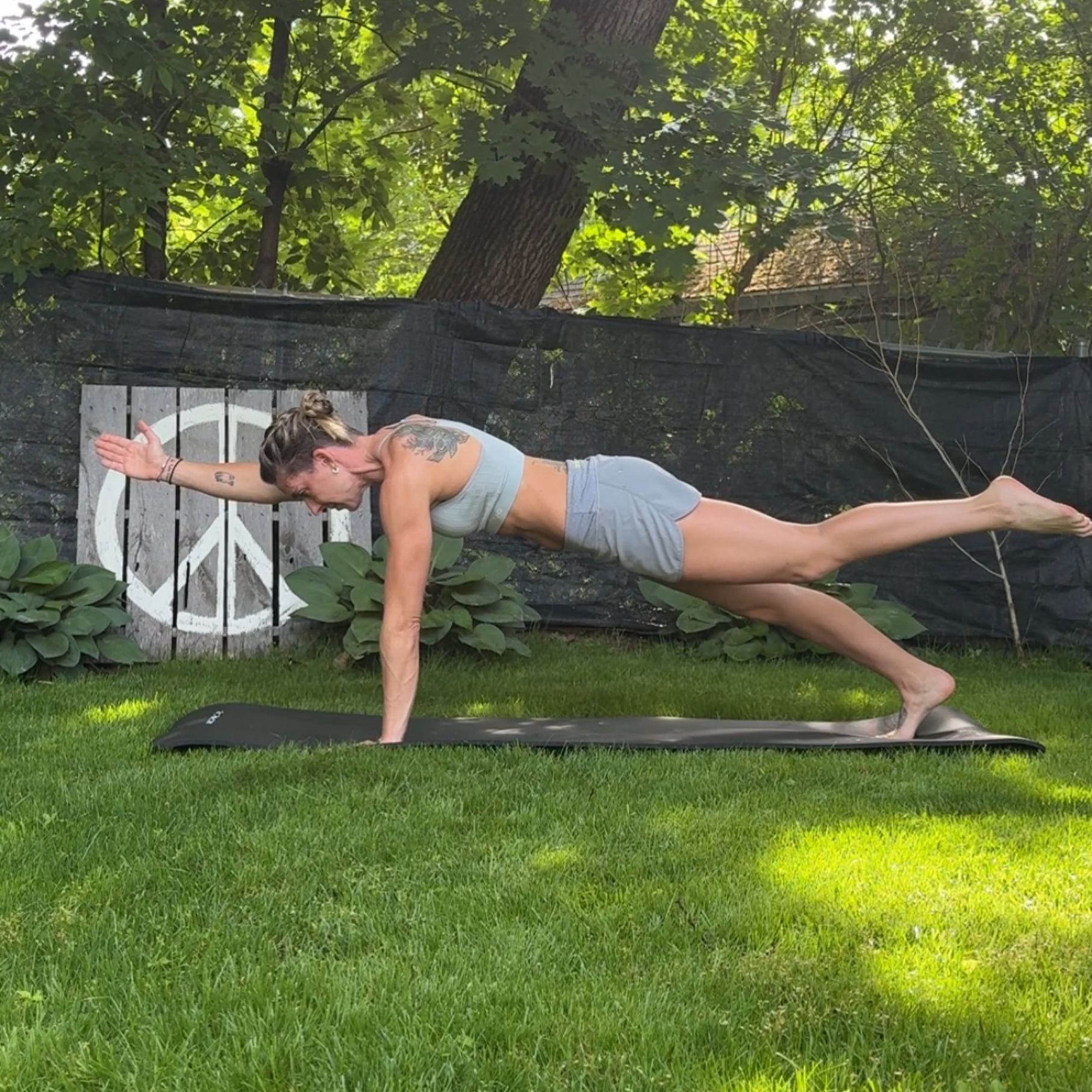A woman does a core exercise on a yoga mat in her backyard.