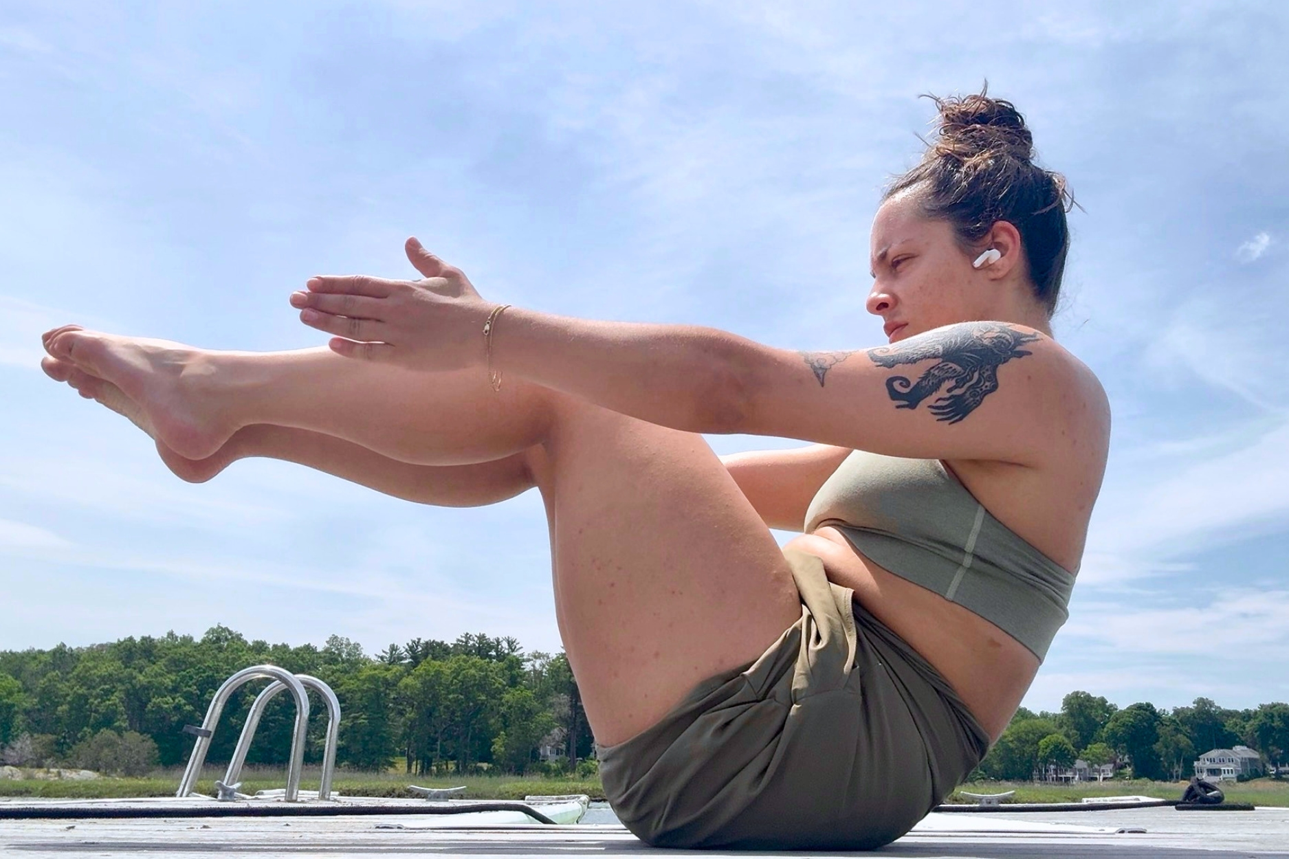 A woman is doing a core workout outside on a dock with trees in the background.