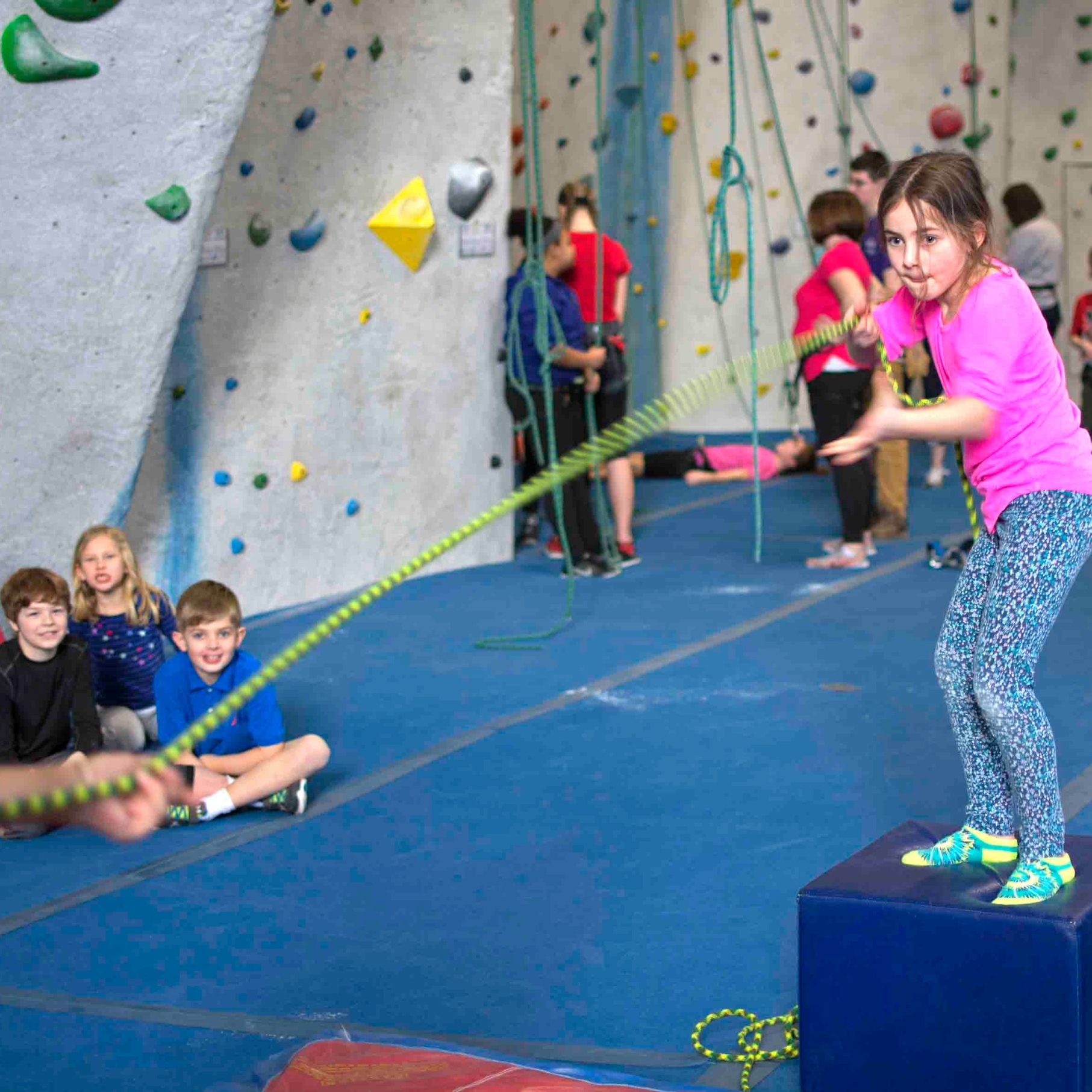 Young girl plays tug of war during summer camp at central rock gym worcester as other camppers cheer her on.