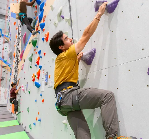 A man is clipped into an auto belay and is reaching up to the next hold.