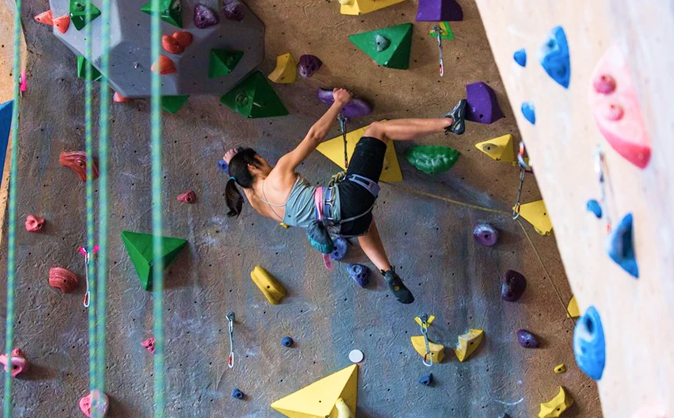A woman is lead climbing on a steep part of the wall. She has cut loose with one foot.
