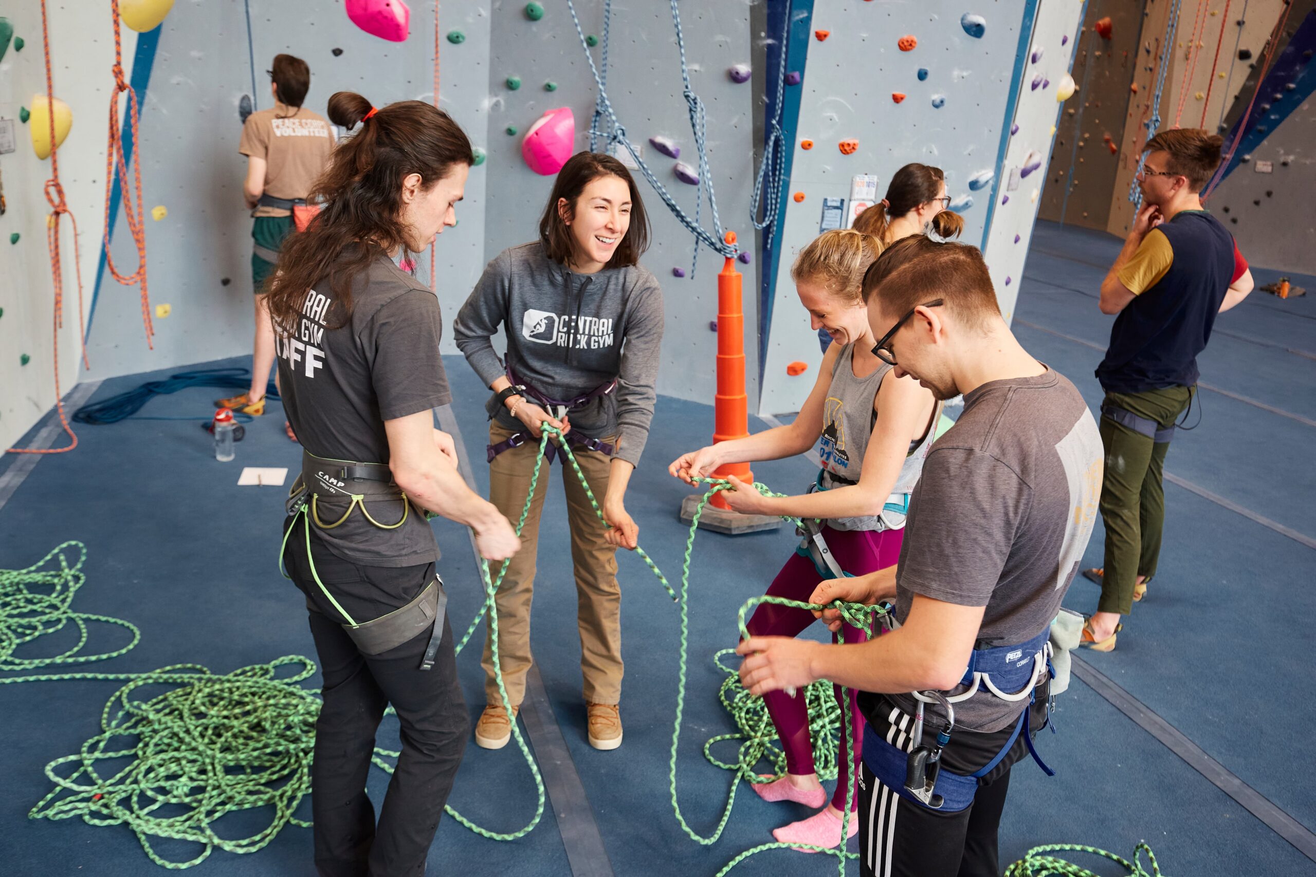 Two Staff members teach two climbers how to tie the figure 8 knot and laugh together.