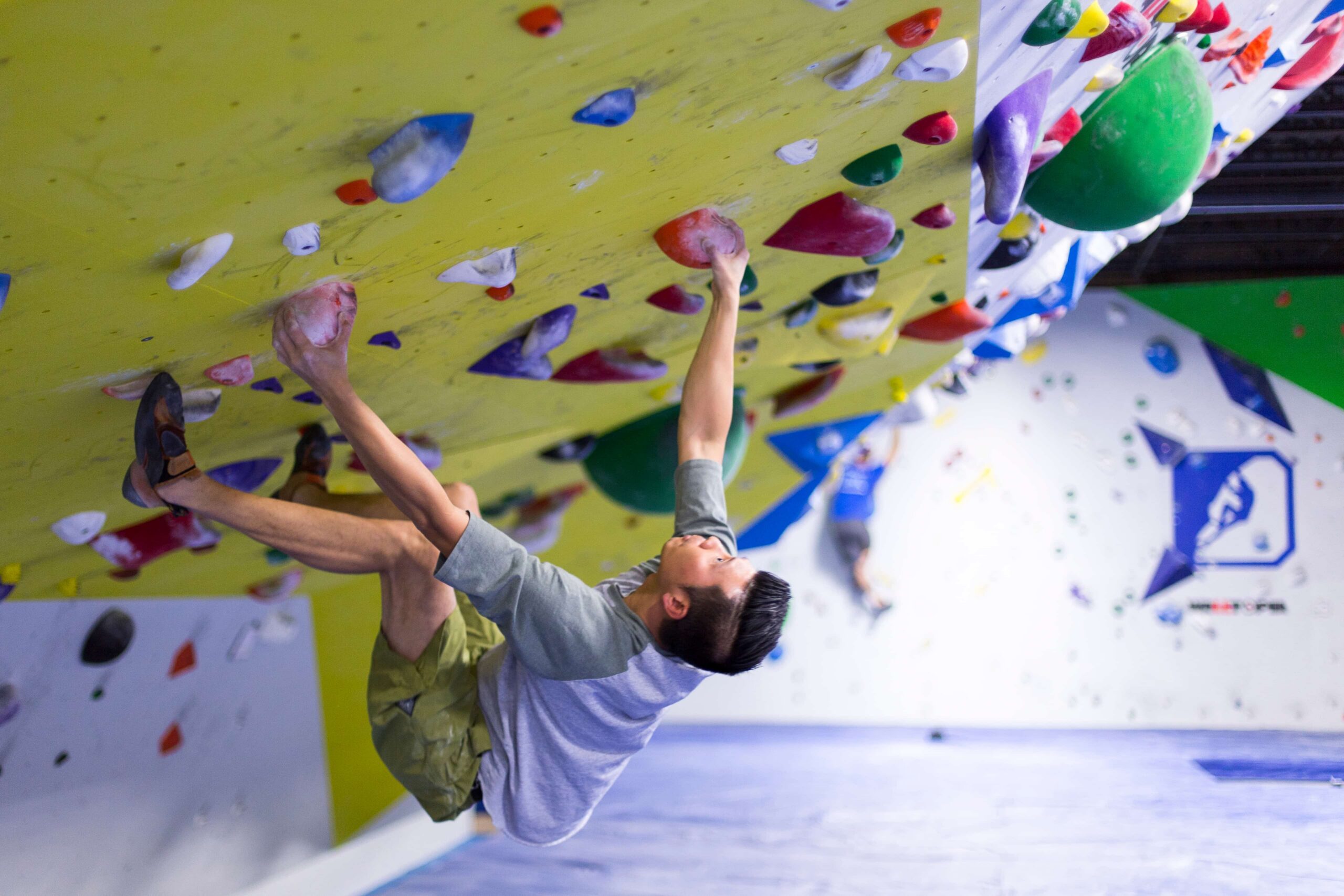 A man with spiked up hair holds onto two slopers on an extremely steep bouldering wall.