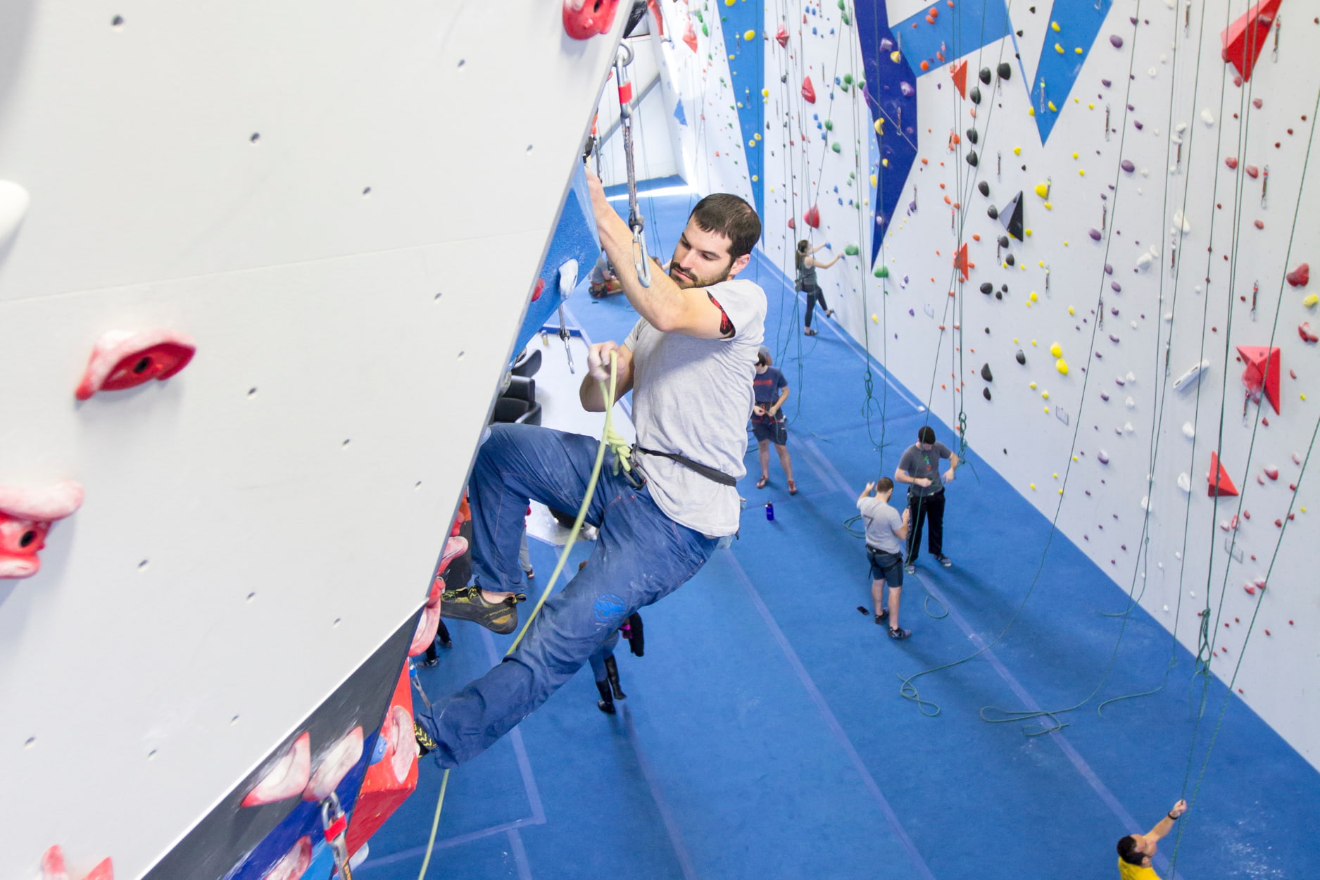 A man is locked off as he pulls the rope up with his other hand to clip it into the next draw on the wall.