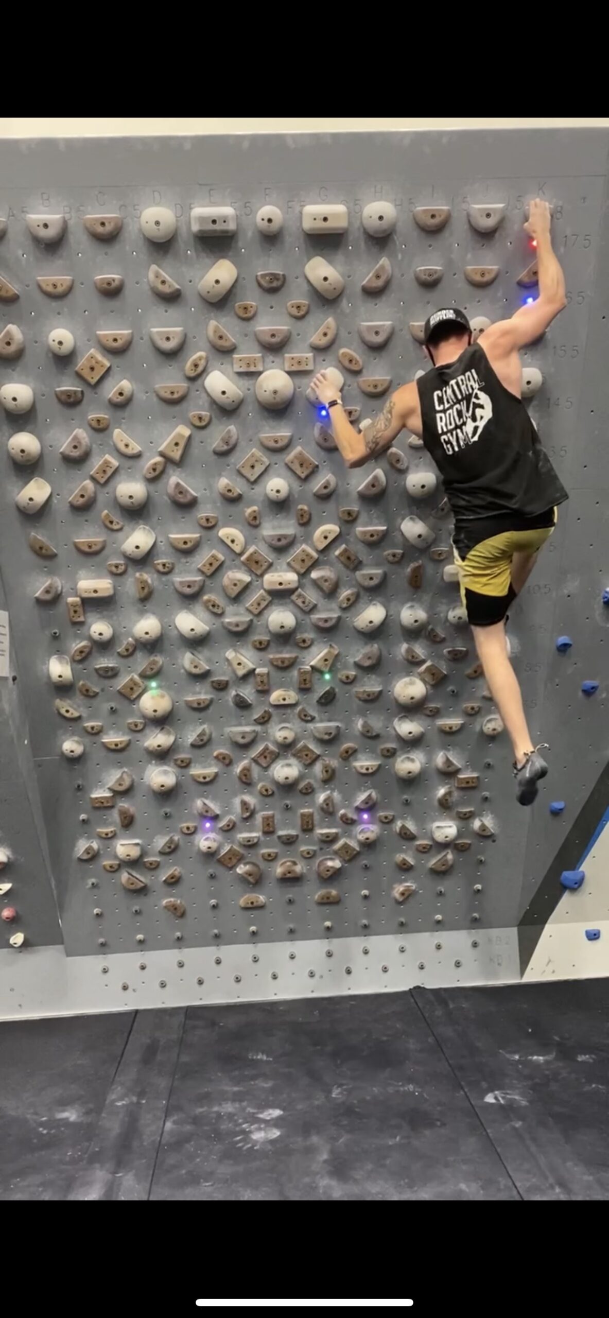A man wearing a backwards cap and CRG tank top climbs on the Tension Board 1