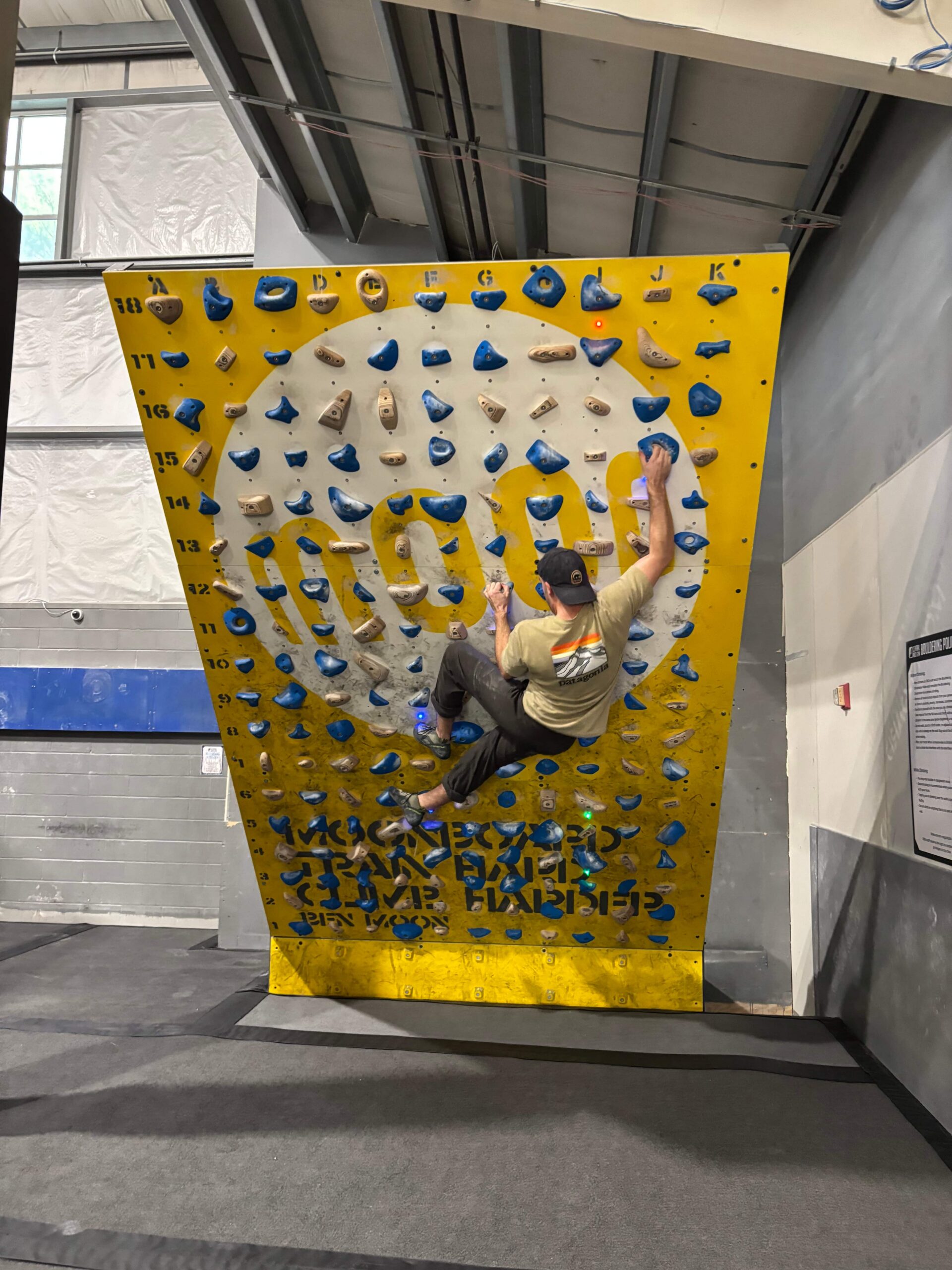A man with a backwards hat climbs on the moonboard.