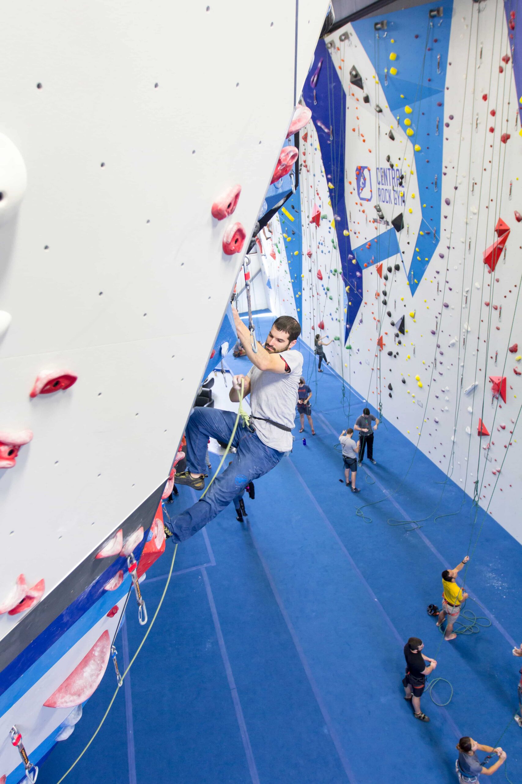 A man is locked off as he pulls the rope up with his other hand to clip it into the next draw on the wall.