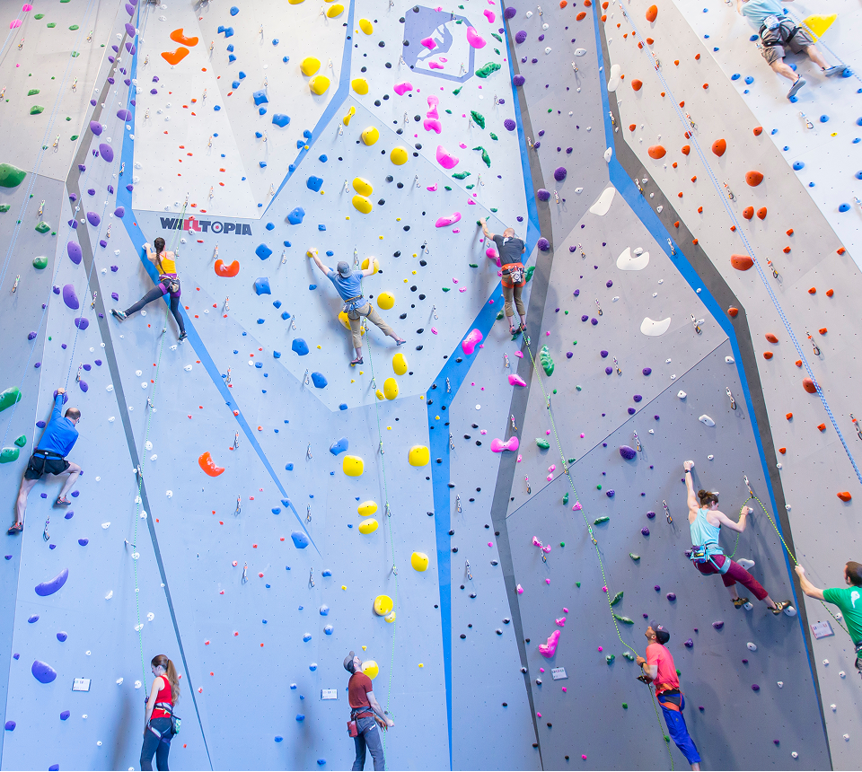 Indoor rock climbing wall with colorful holds and six climbers in various positions. They exhibit focus and determination, creating an energetic atmosphere.