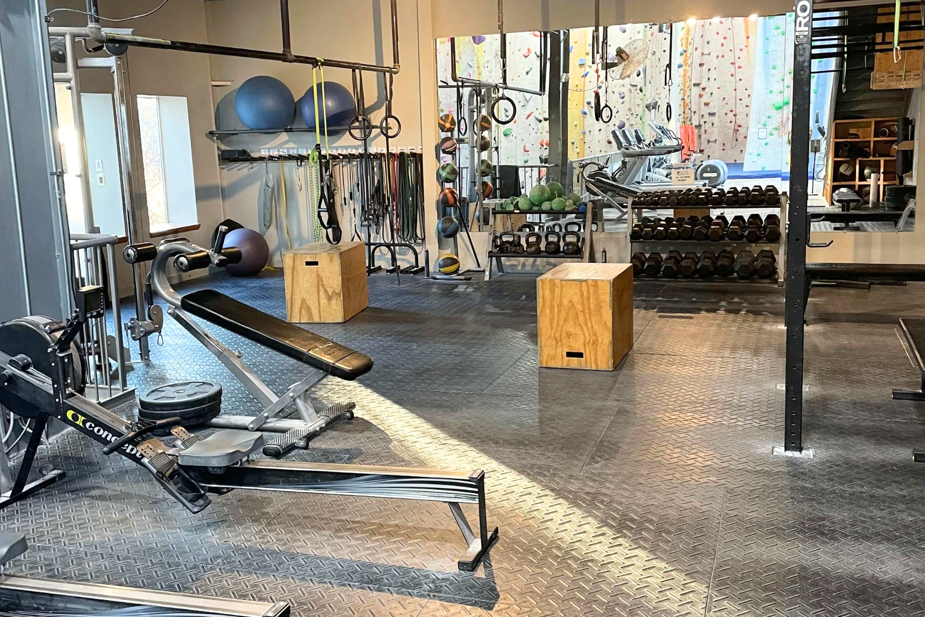 Fitness equipment in a climbing gym including a rower, dumbbells, a box, benches, rings, and more.