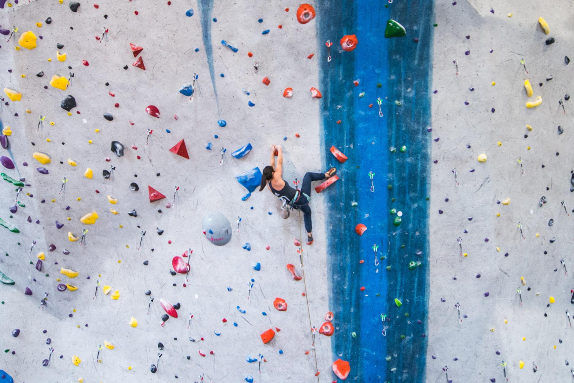 A woman lead climbs on a huge rope wall. She places a high heel hook on the wall and matches hands.