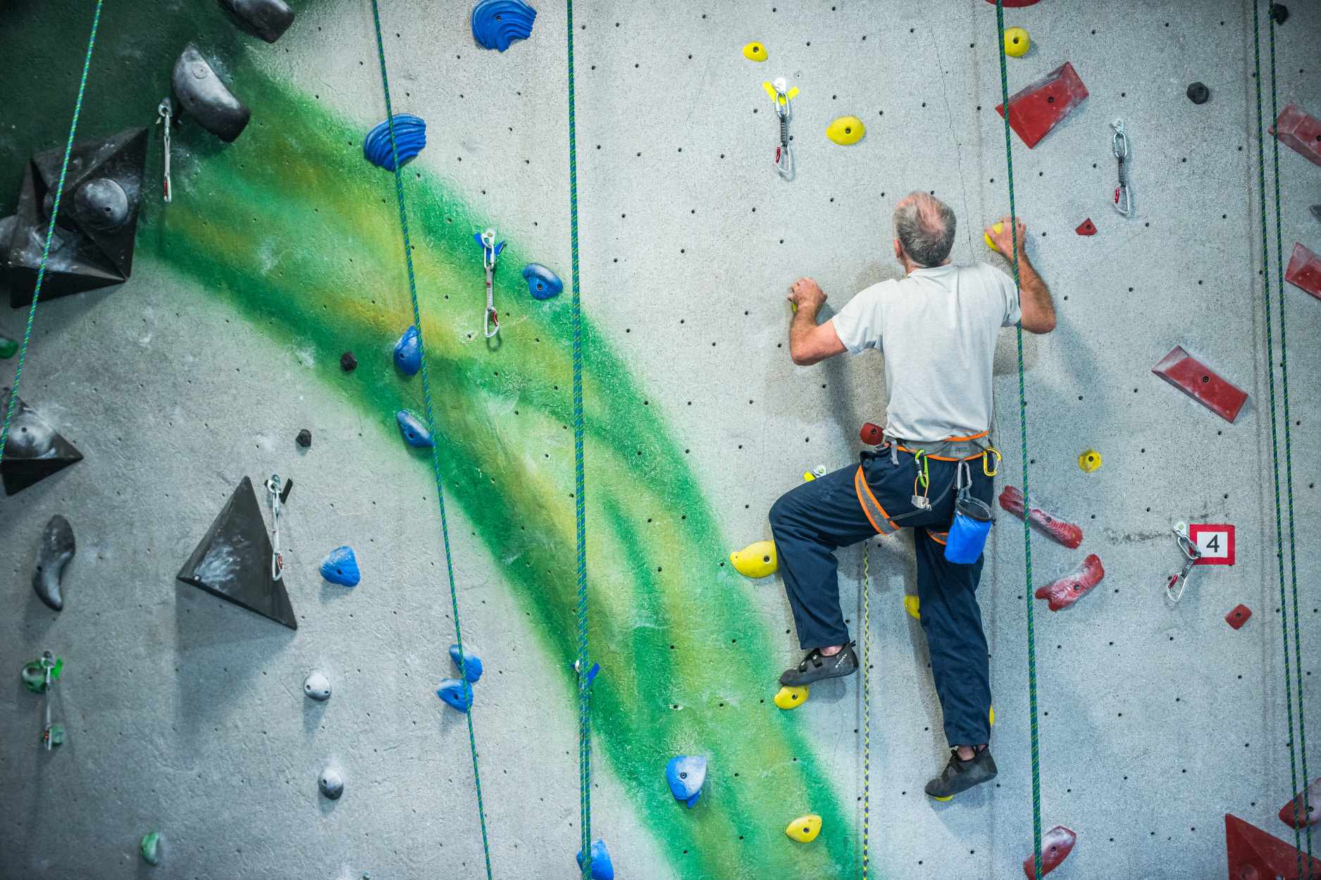 An older gentleman is lead climbing up a vertical wall on a moderate climb at Central Rock Gym.