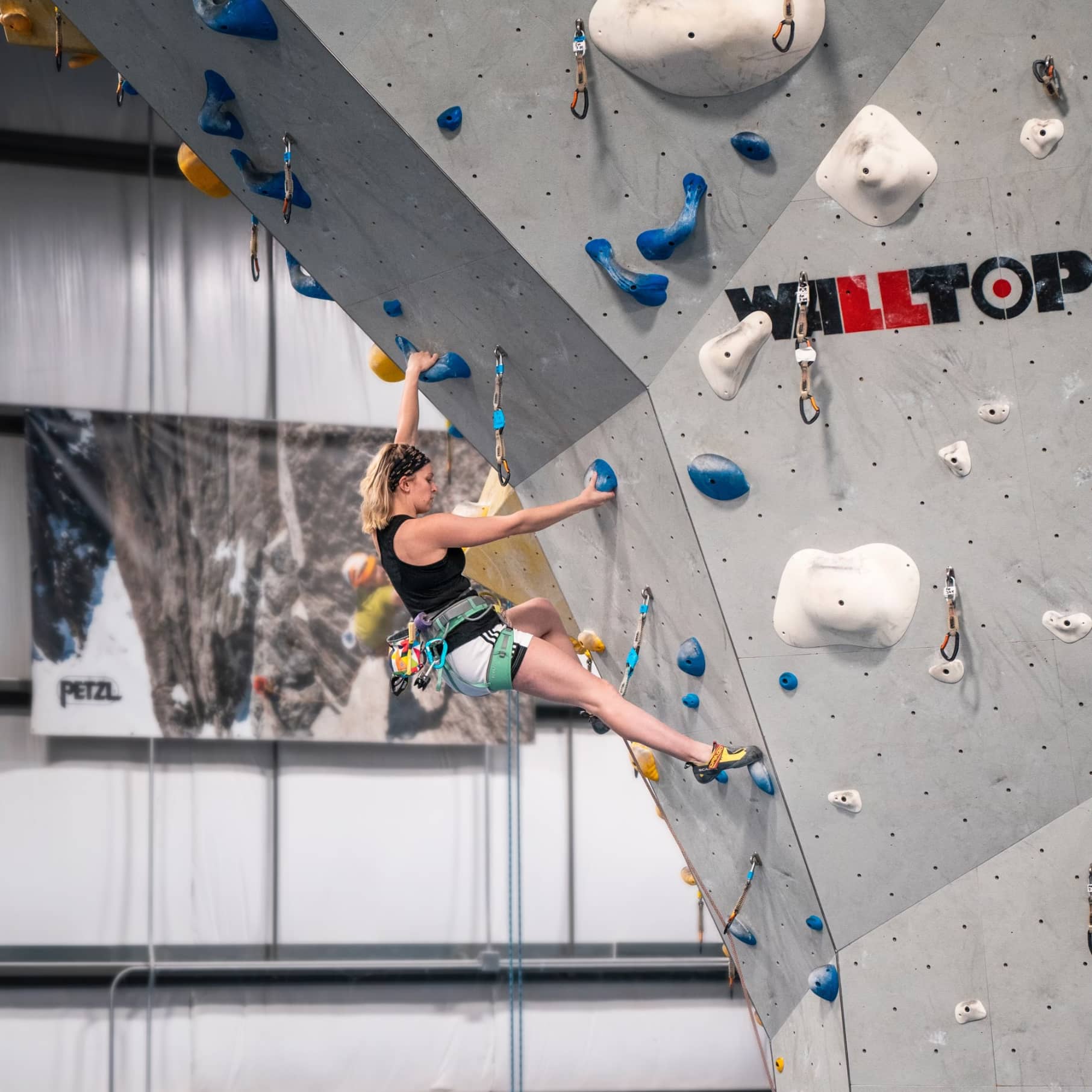 A woman is lead climbing at Central Rock Gym. She has short shoulder length stright hair and a headband.