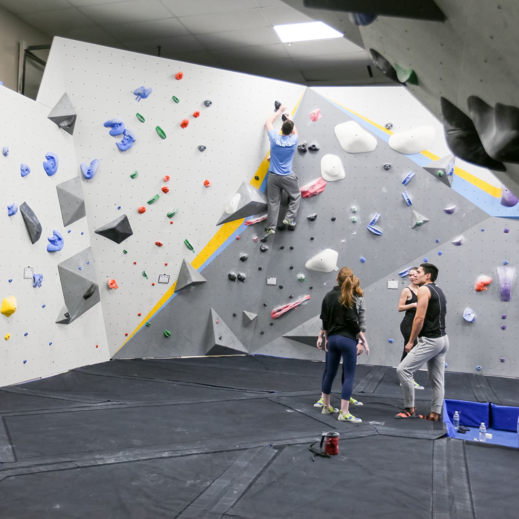 a man bouldering while people below watch at central rock gym