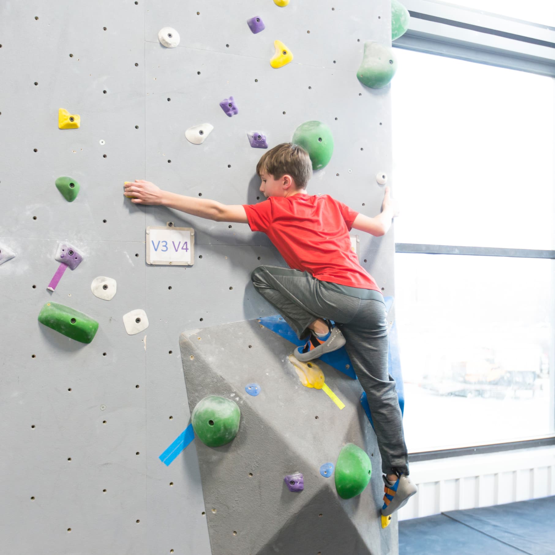 A young boy is bouldering at central rock gym