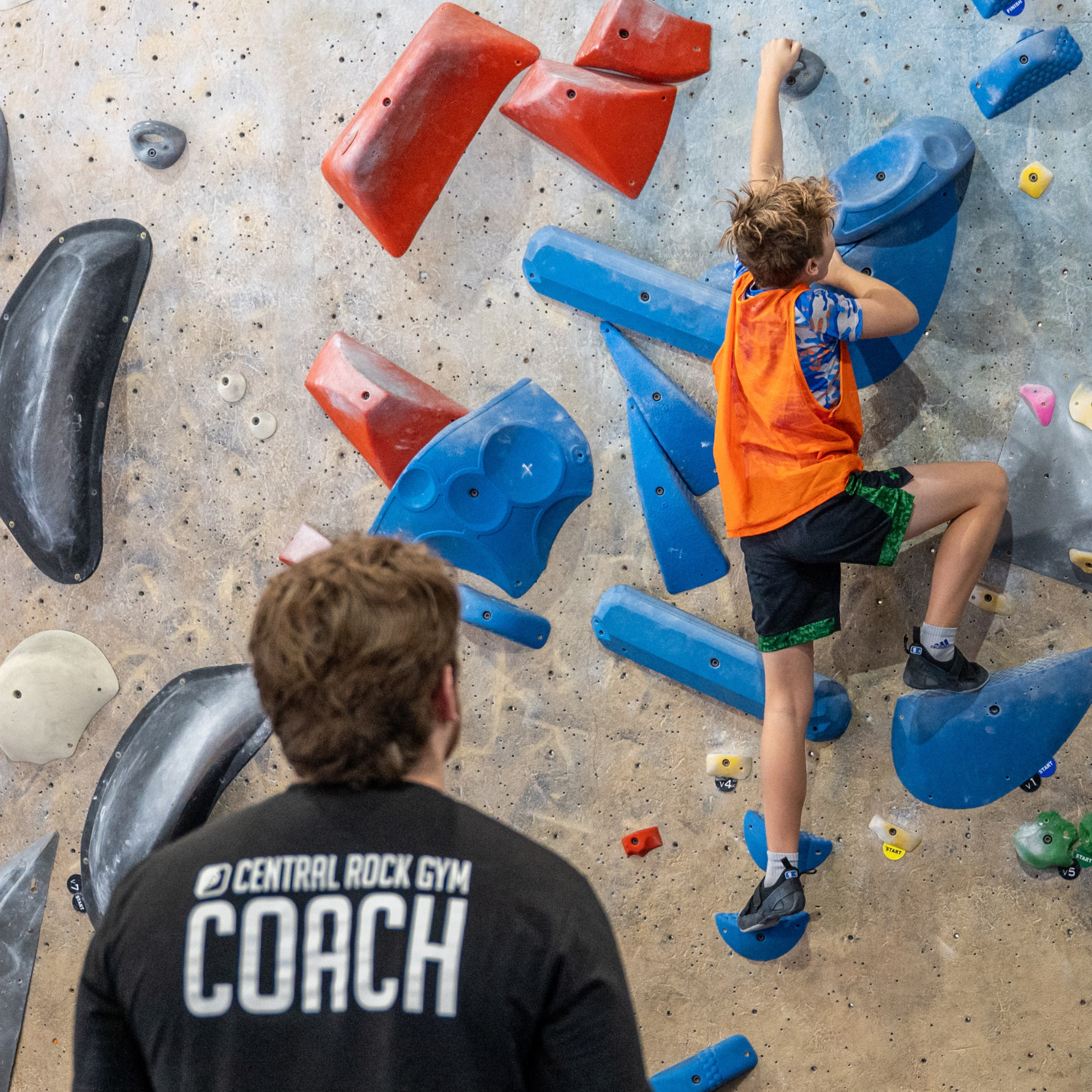 A coach watches a young boy bouldering during a youth program at Central Rock Gym.