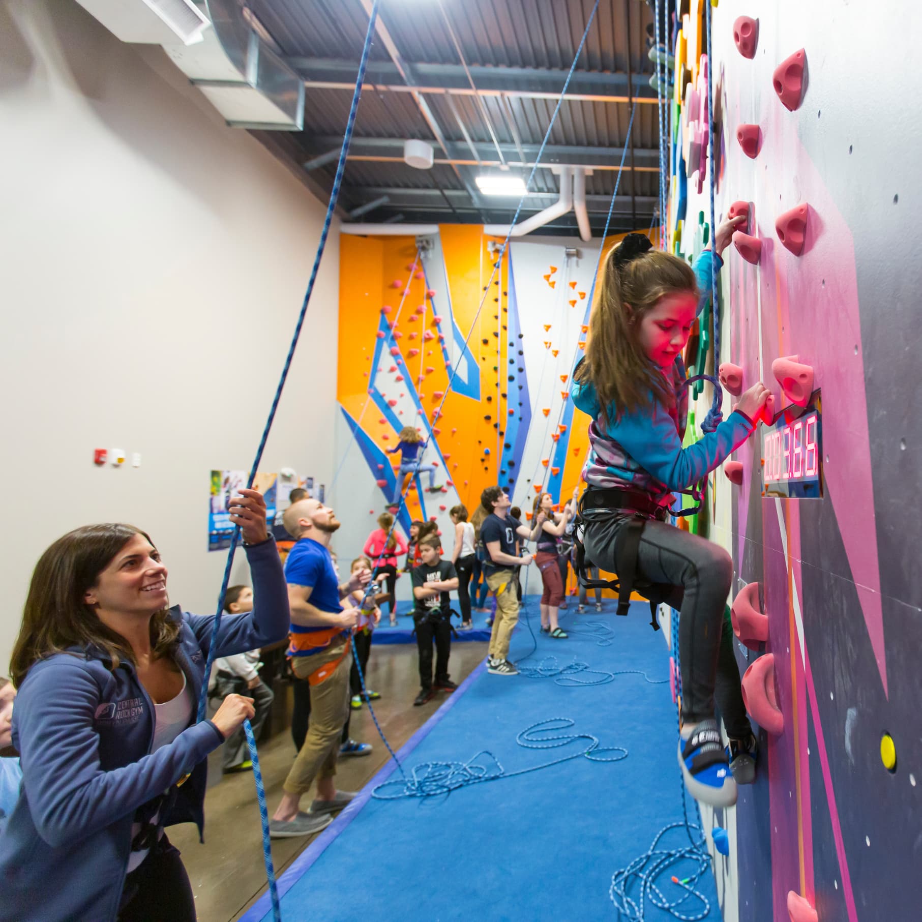A little girl is being spotted while top rope climbing at central rock gym