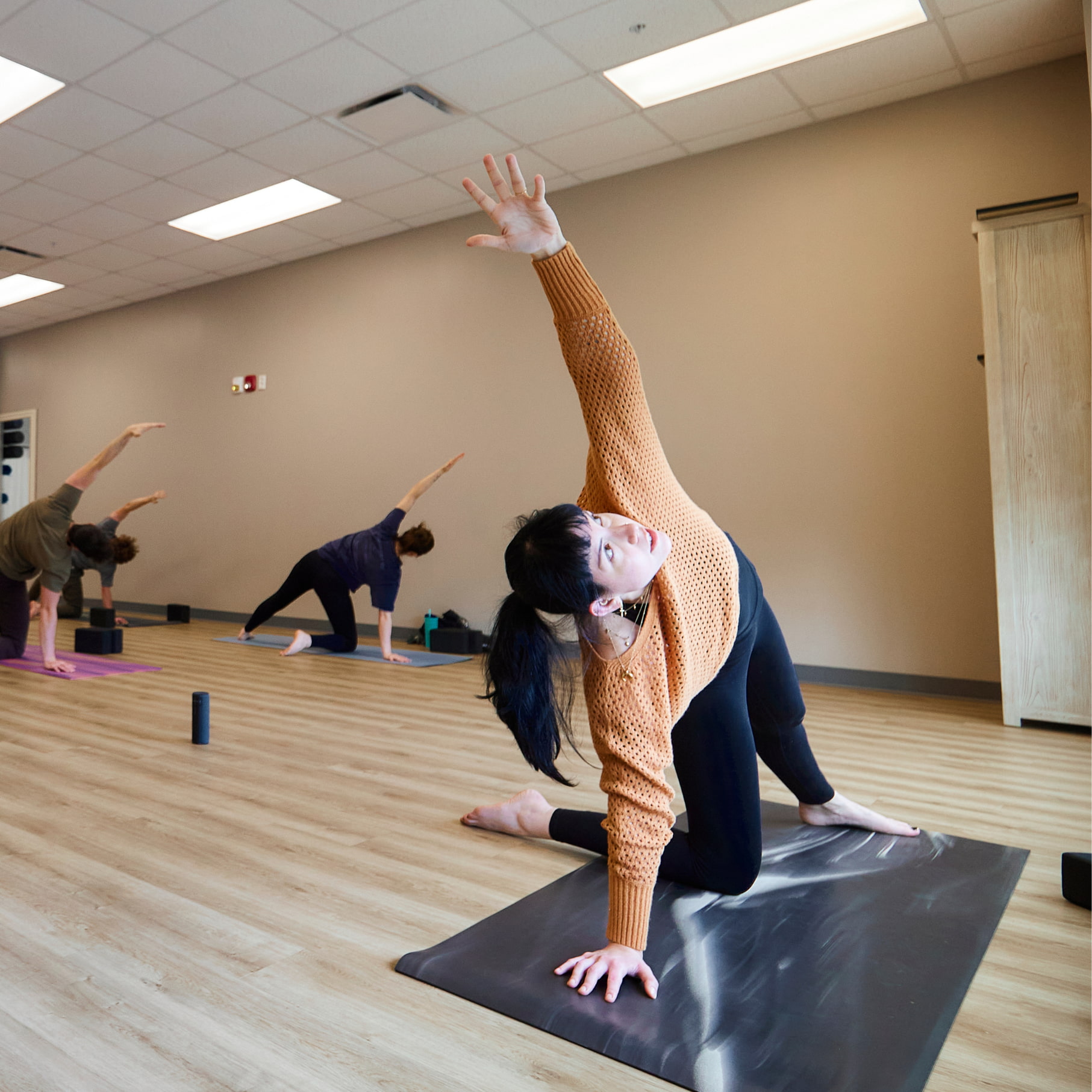 A yoga instructor wearing a loose sweater leads the class in a flow.