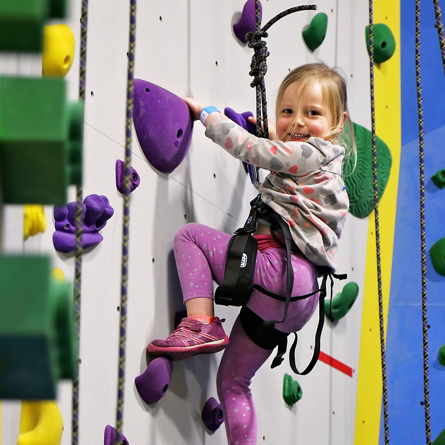 A little girl is top rope climbing at central rock gym
