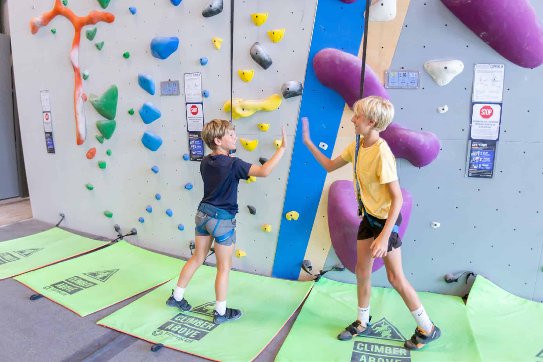 Two boys high five as they stand clipped into an auto belay climbing system at Central Rock Gym.