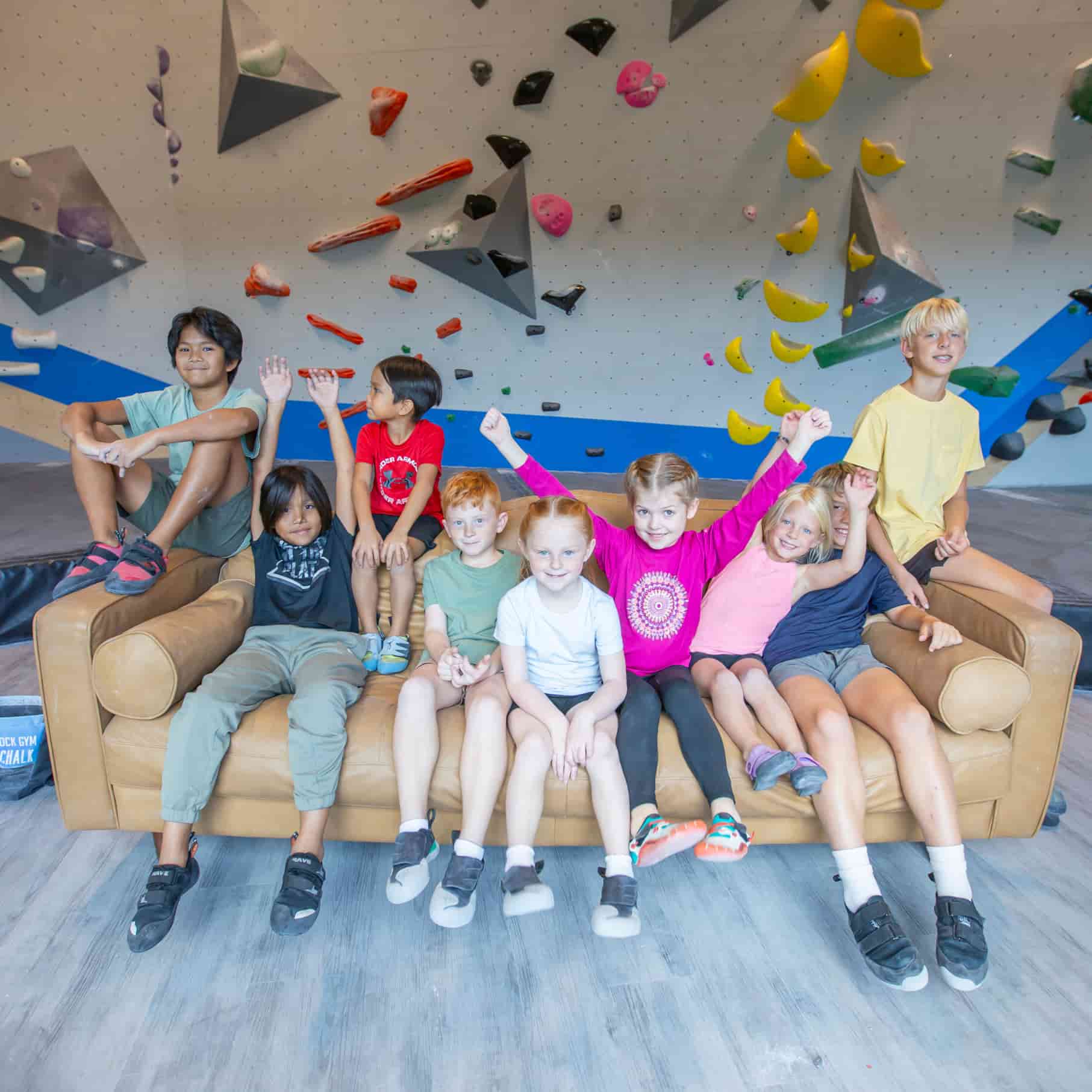 A group of kids sit together on a couch in front of a rock climbing wall at Central Rock Gym.