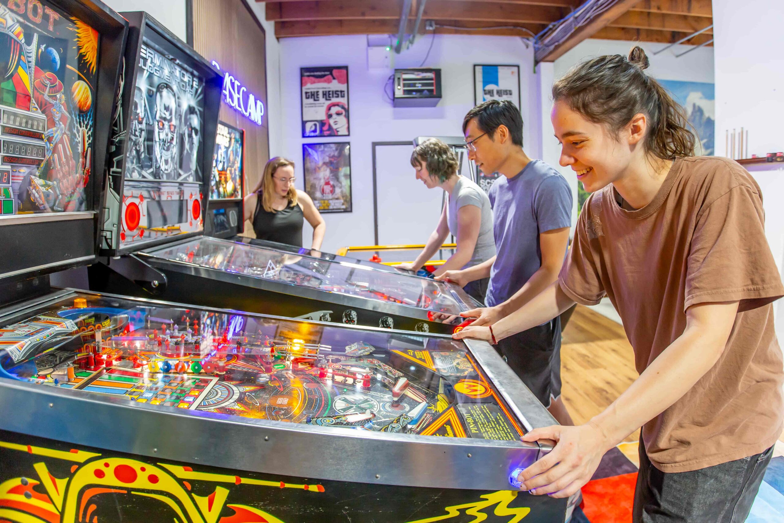 A group of friends play pinball in Basecamp at CRG Watertown.